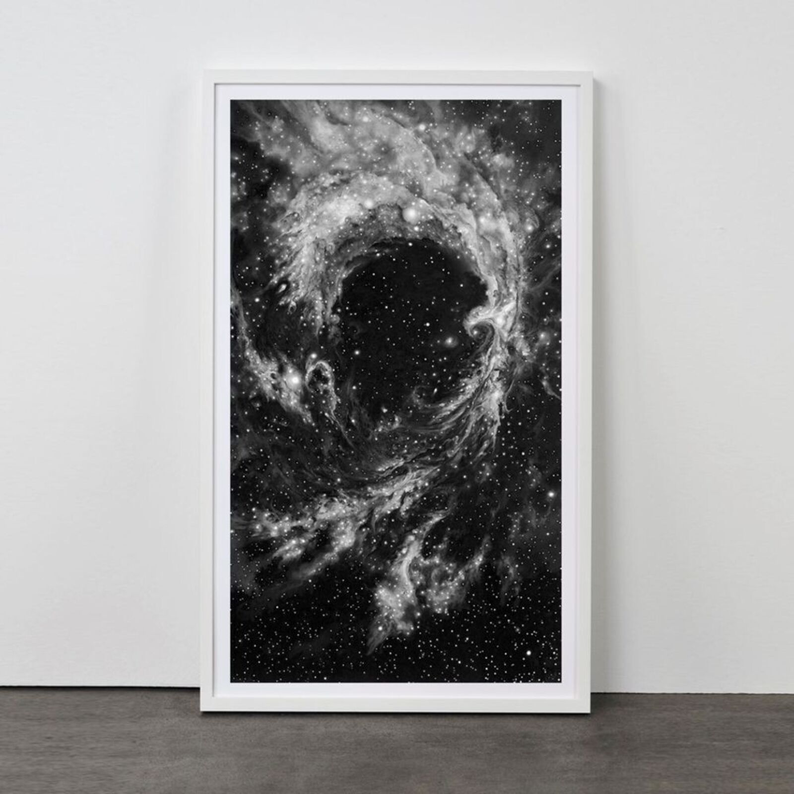 A framed black-and-white print of a swirling cosmic nebula against a minimalist interior wall.