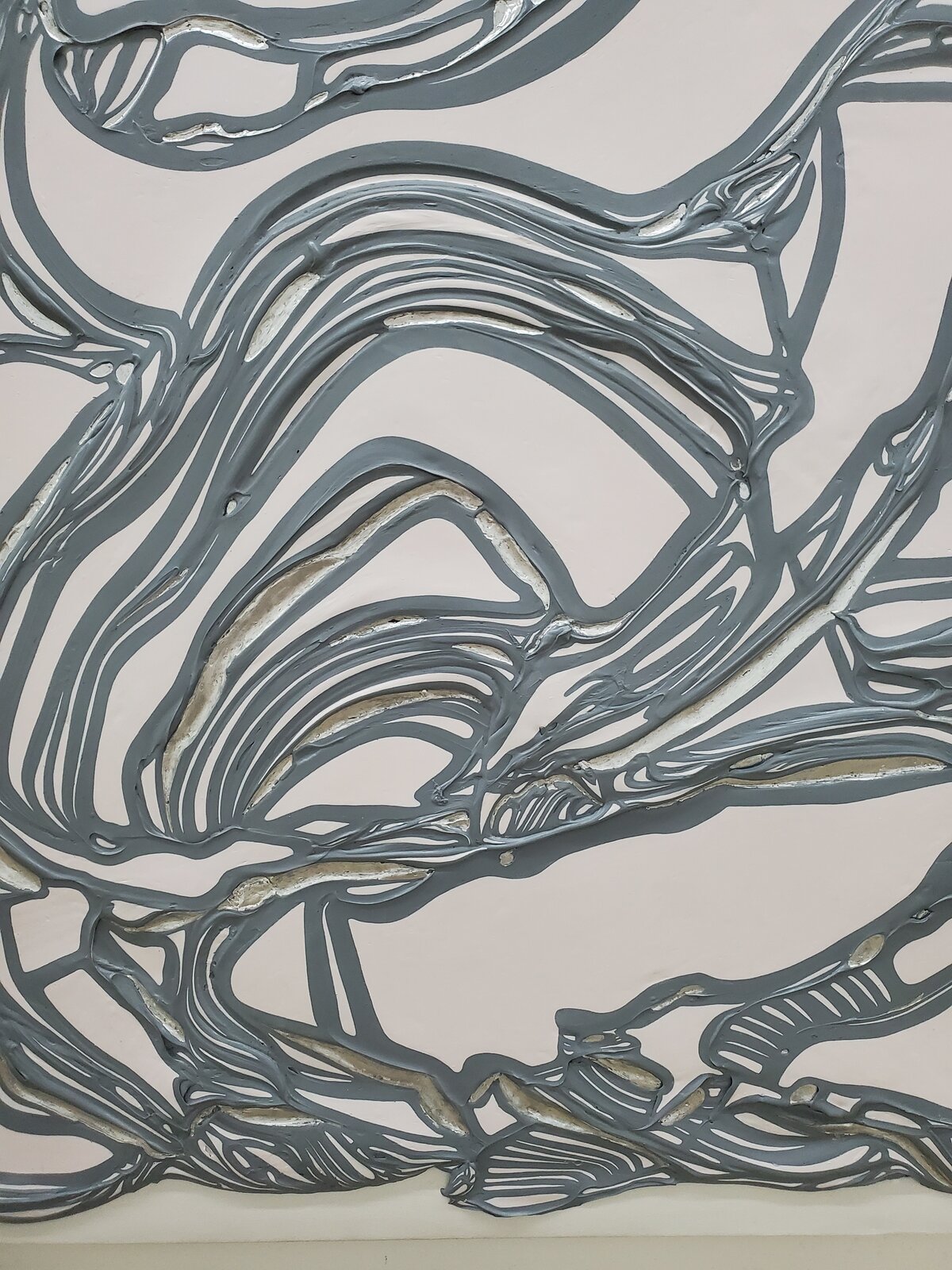 A textured abstract relief featuring a network of grey, ribbon-like forms against a pale background.