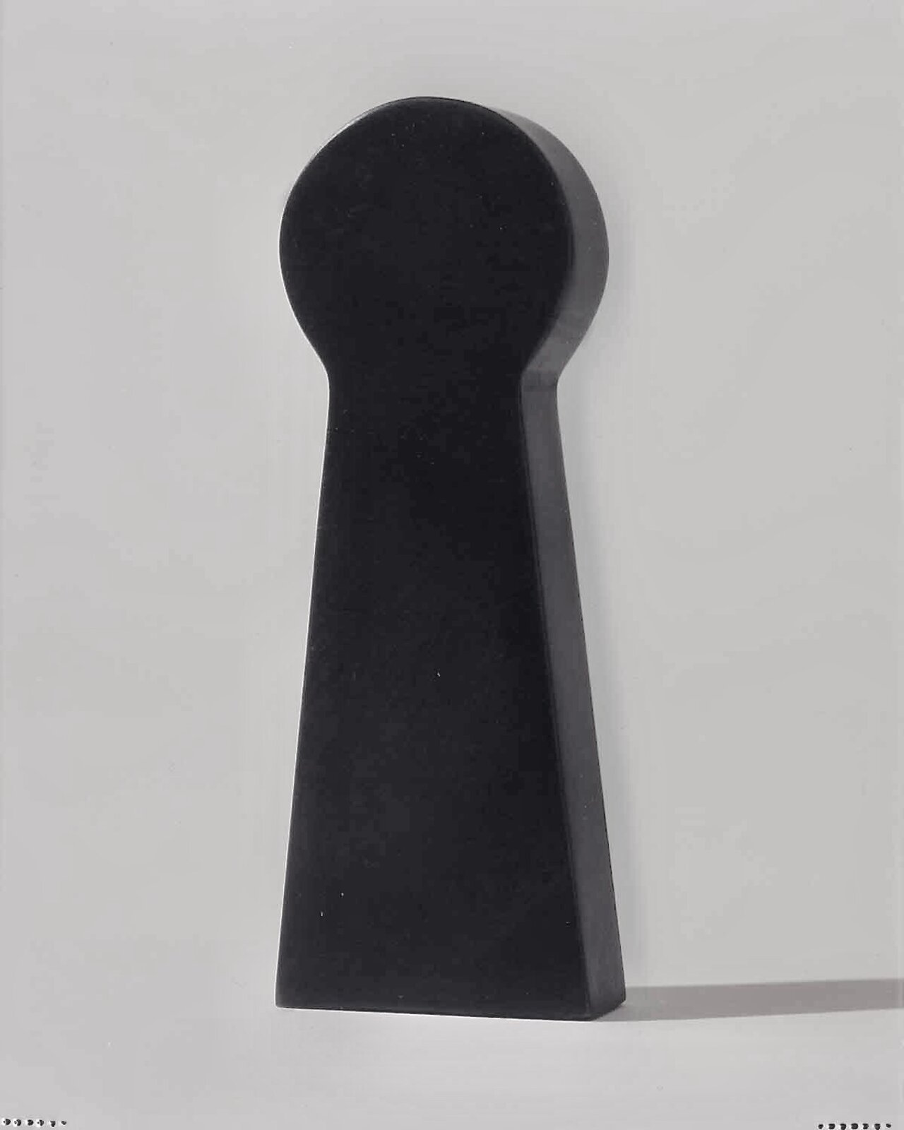 A minimalist black sculpture shaped like a keyhole against a stark white background.