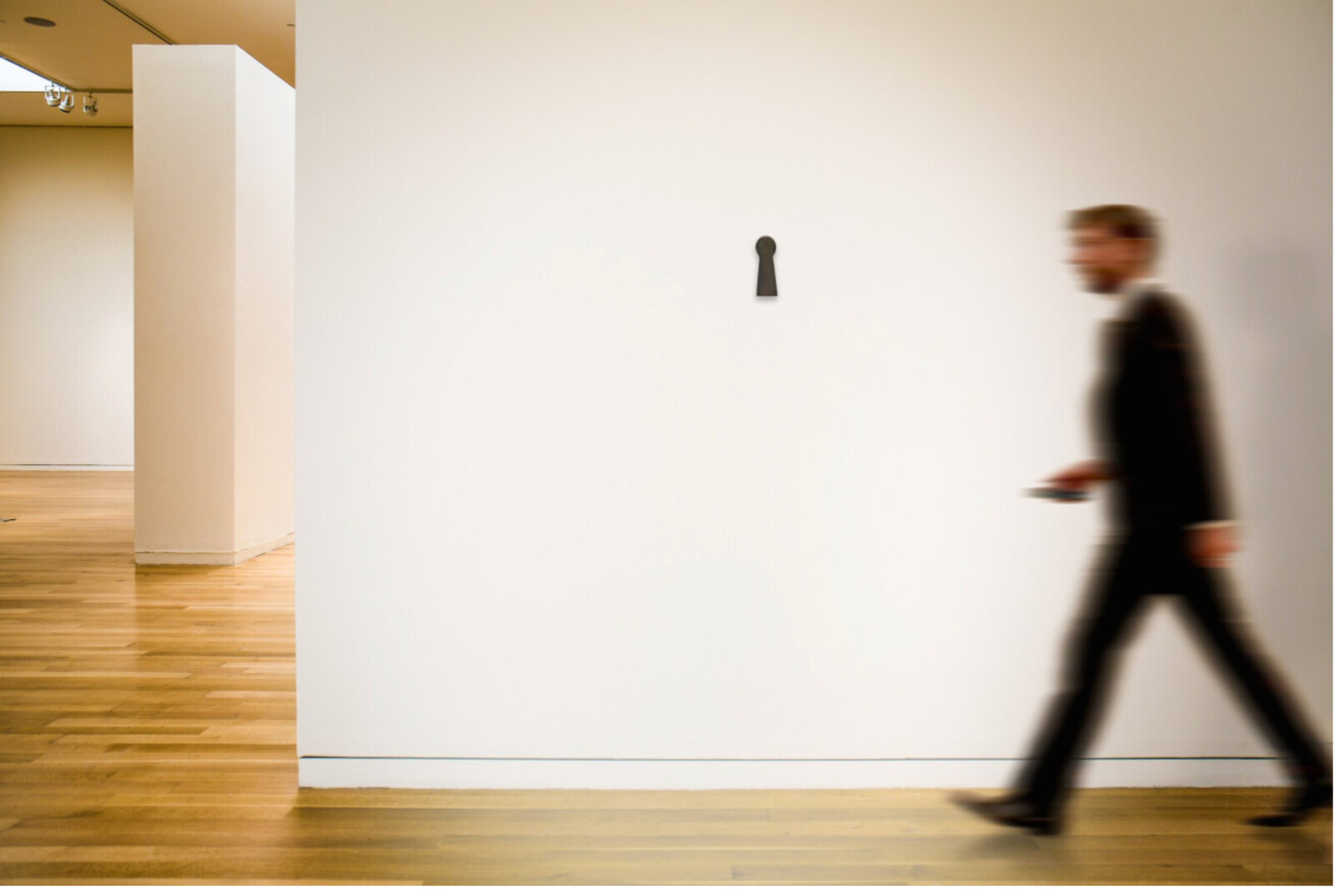A minimalist black sculpture shaped like a keyhole against a stark white background.