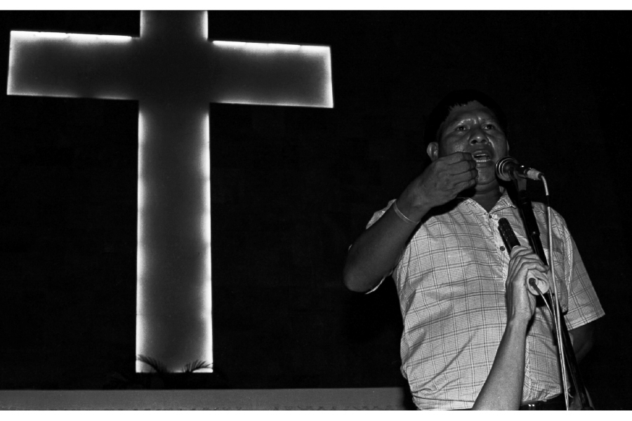 A man holding a microphone in front of a cross.
