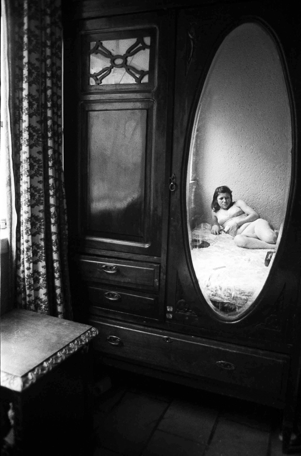 A black and white photo of a woman laying on a bed in front of a mirror.