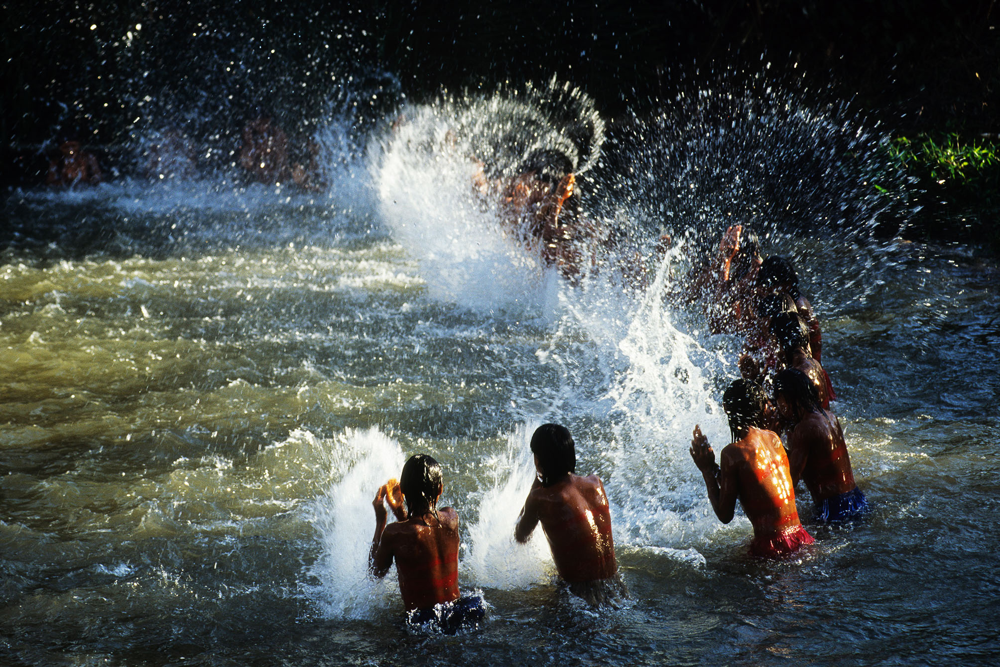 A group of people playing in a river with water splashing around them.