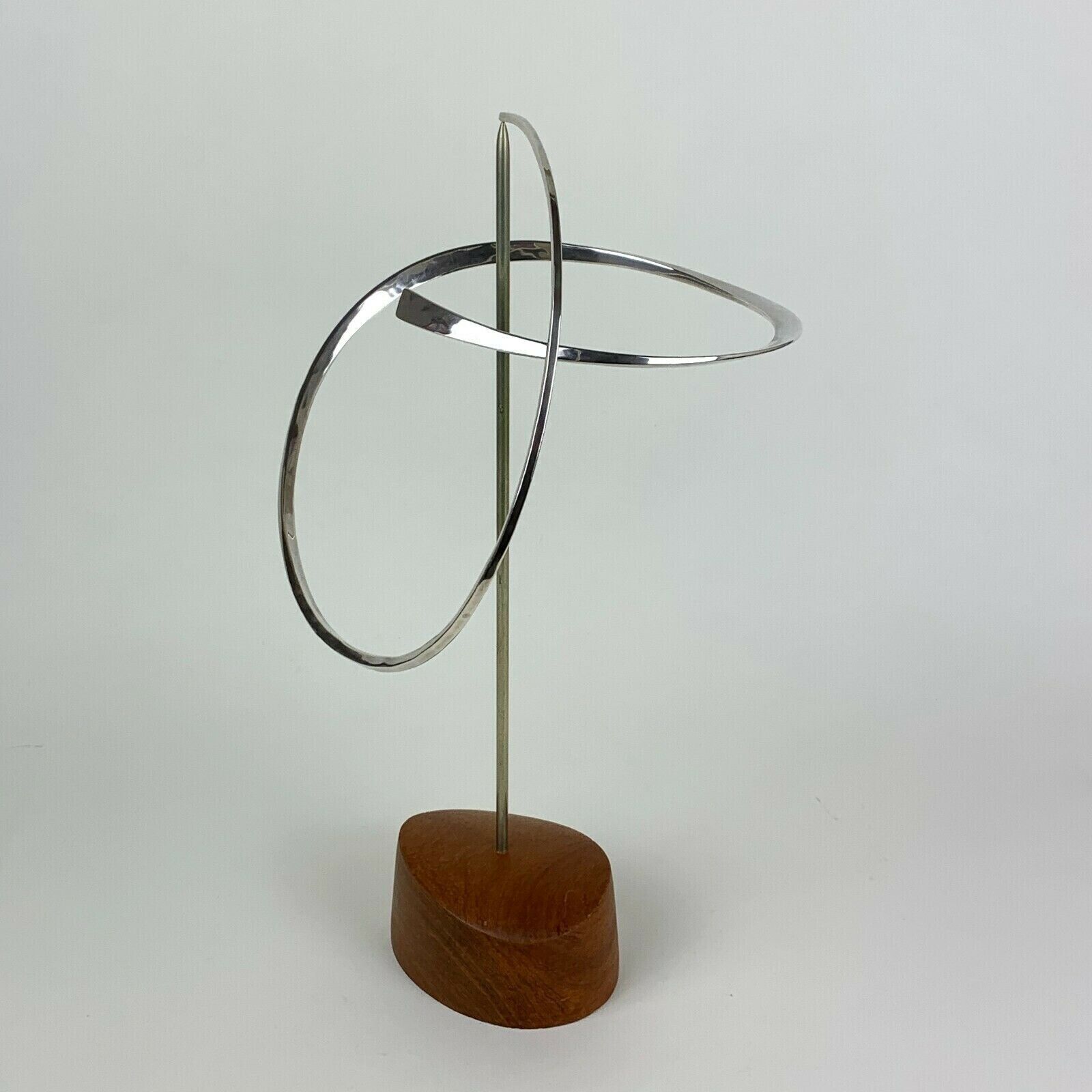 A silver bangle on a wooden stand on a white background.