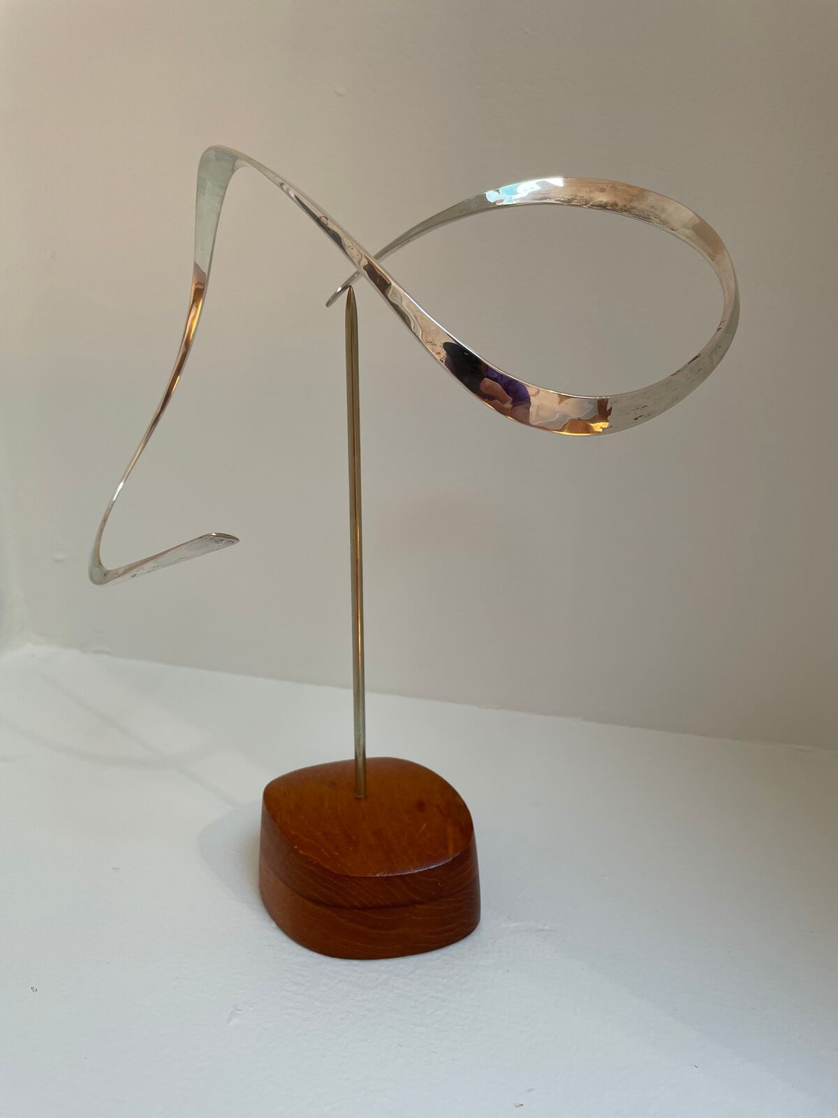 A silver sculpture on a wooden stand on a white surface.