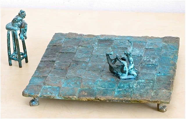 A bronze sculpture of a man sitting on a stool next to a chess board.