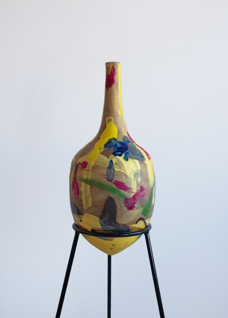 A yellow vase sitting on top of a metal stand.
