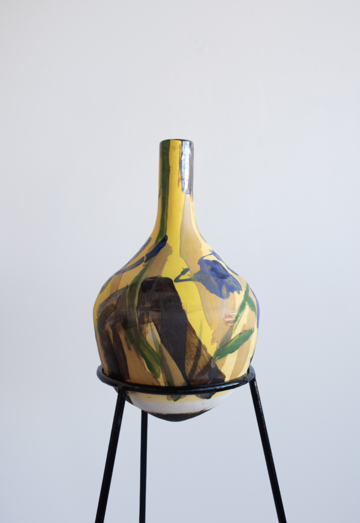 A yellow vase sitting on top of a metal stand.