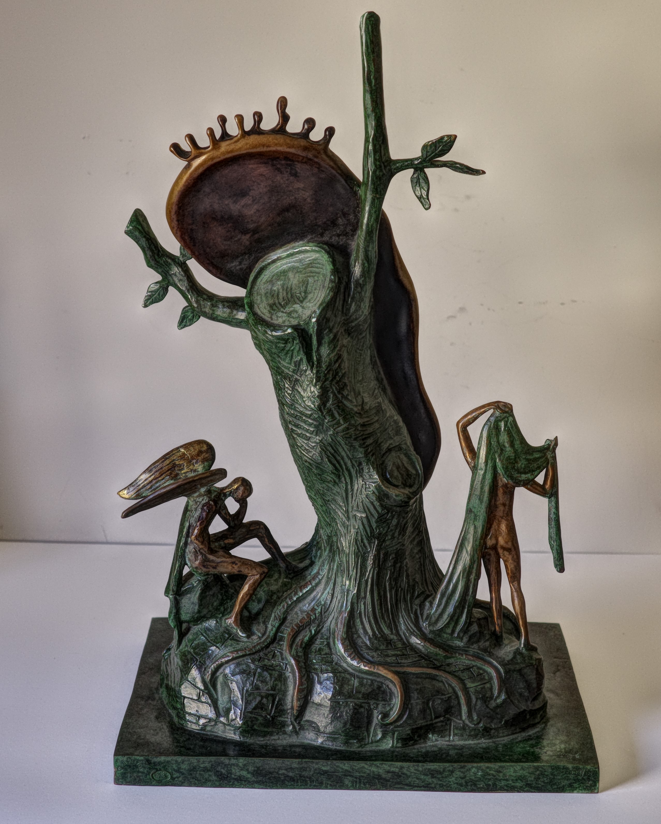 A bronze sculpture of a clock on top of a tree.