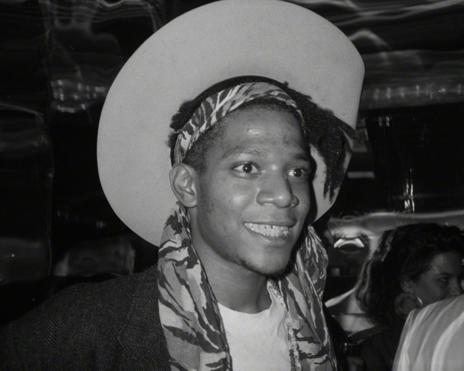 A man wearing a hat and a scarf smiles at the camera.