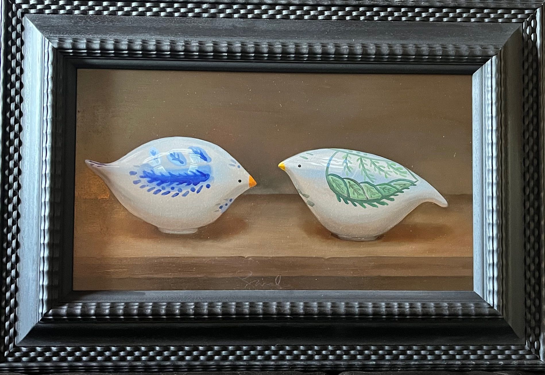 A framed diorama featuring two ceramic bird figures facing each other.