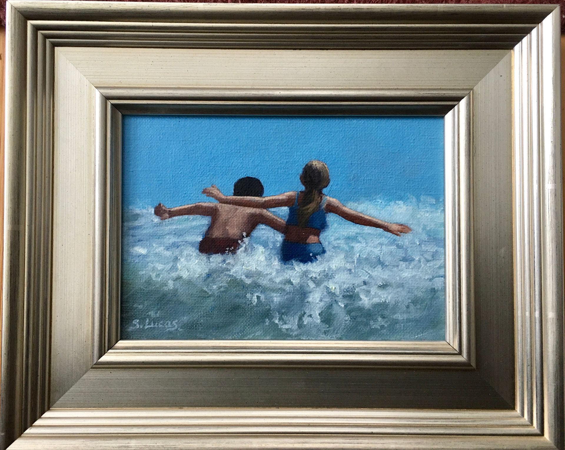 A framed painting of two figures swimming in the ocean with arms outstretched.