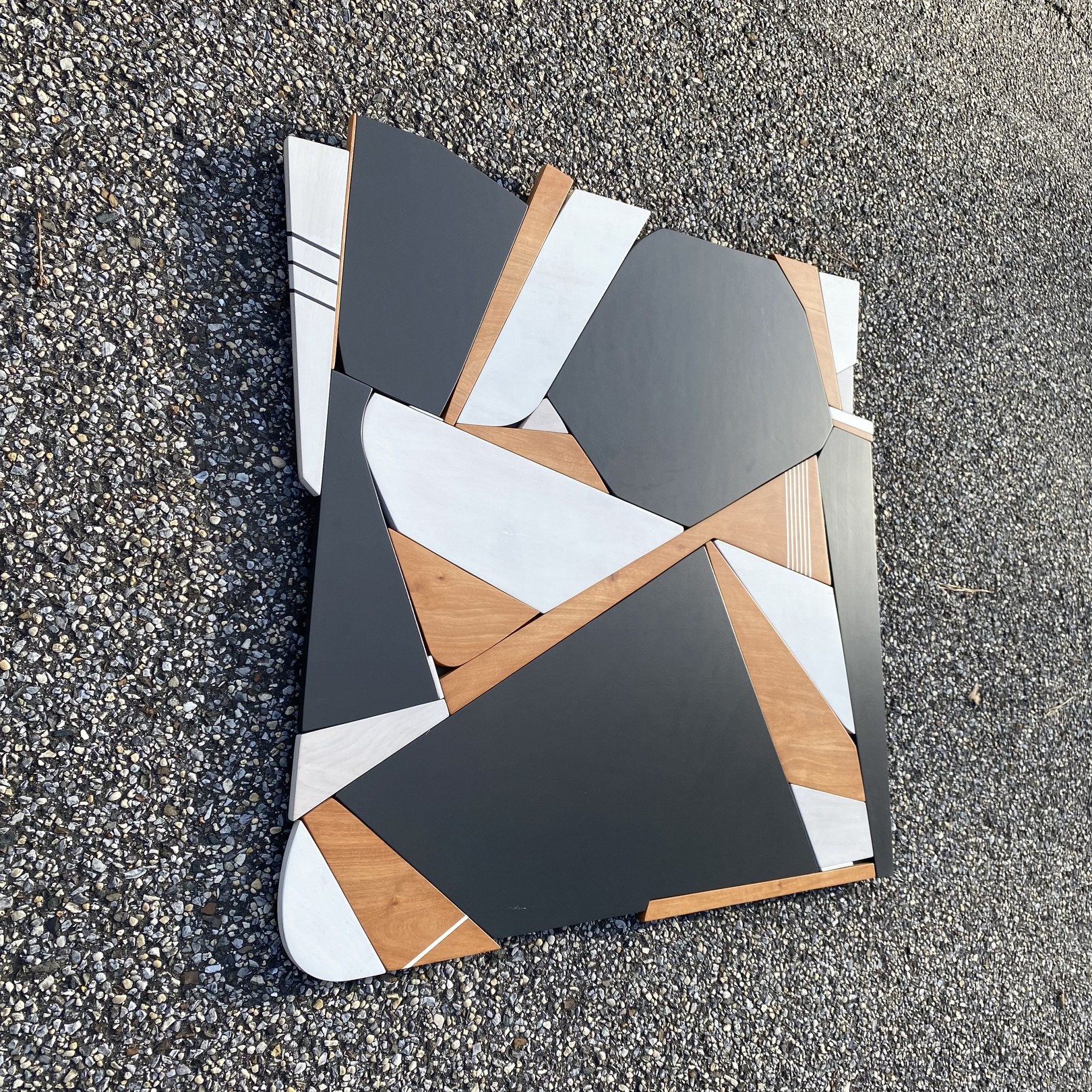 A modern geometric tabletop featuring a mosaic of dark gray, white, and light wood panels arranged in an abstract pattern.