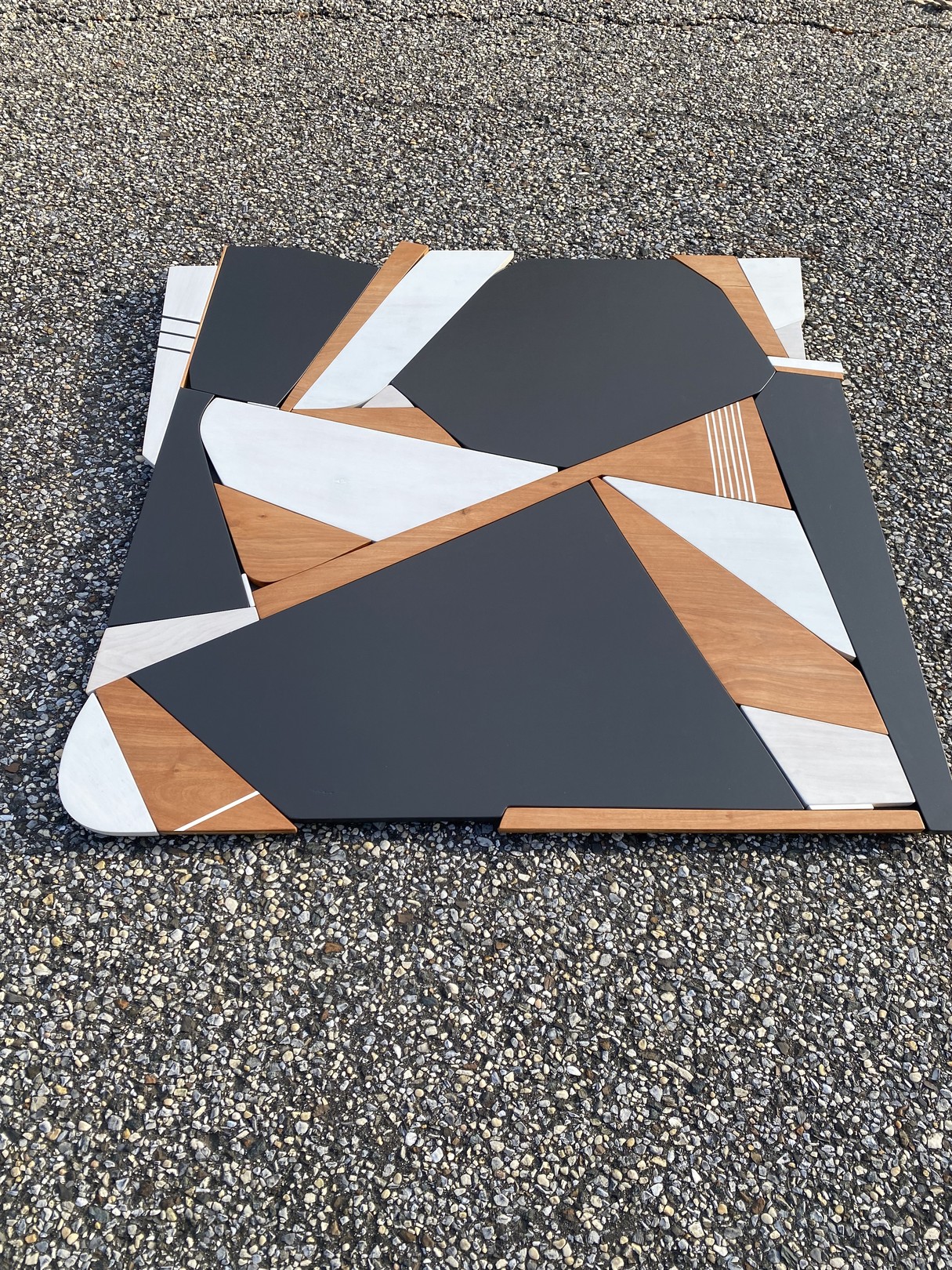 A modern geometric tabletop featuring a mosaic of dark gray, white, and light wood panels arranged in an abstract pattern.