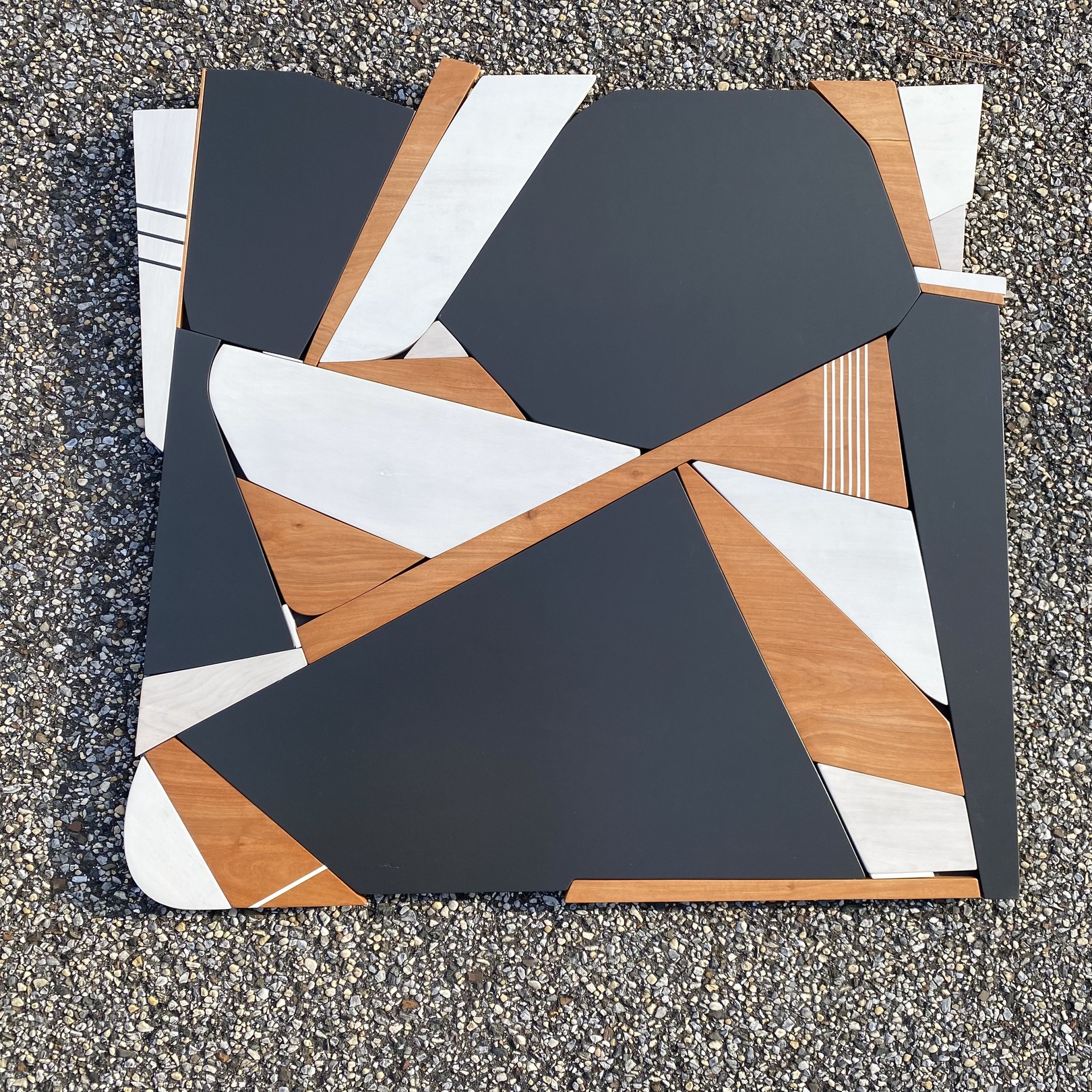 A modern geometric tabletop featuring a mosaic of dark gray, white, and light wood panels arranged in an abstract pattern.