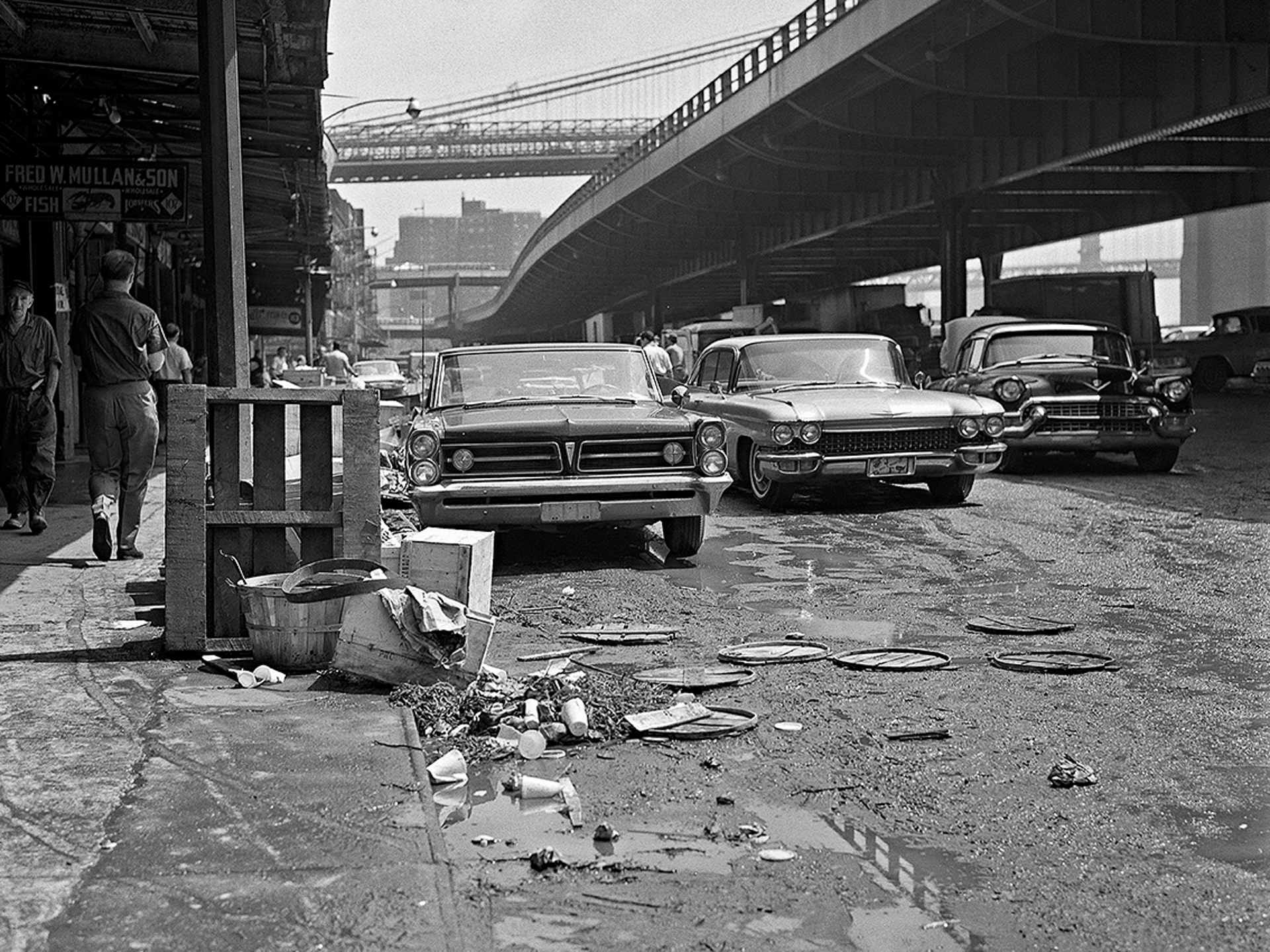 A black and white photo of cars parked on the side of a street.