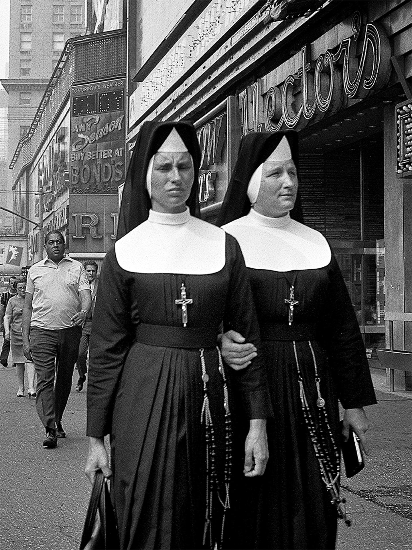 Two nuns walking down the street in front of a store.