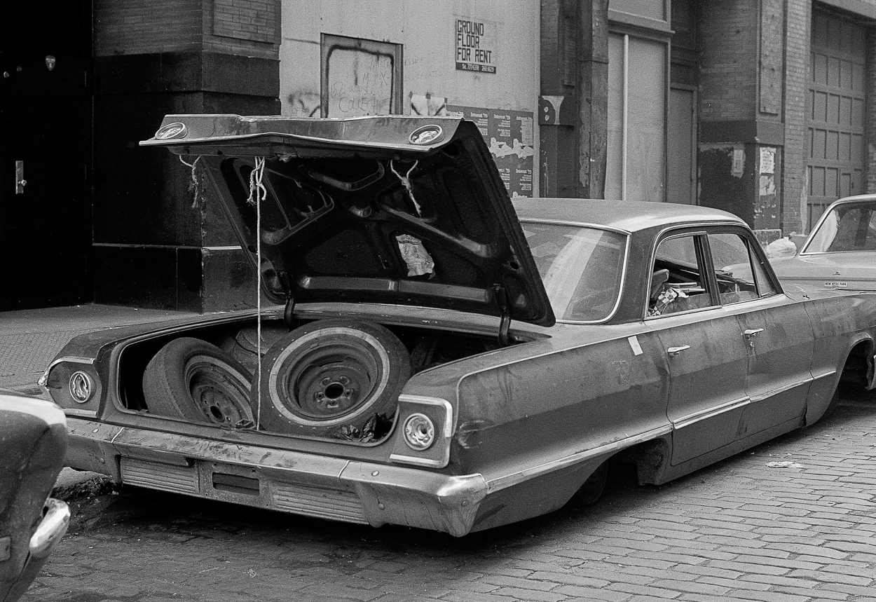 A low-slung classic car with its trunk open, revealing spare tires inside.