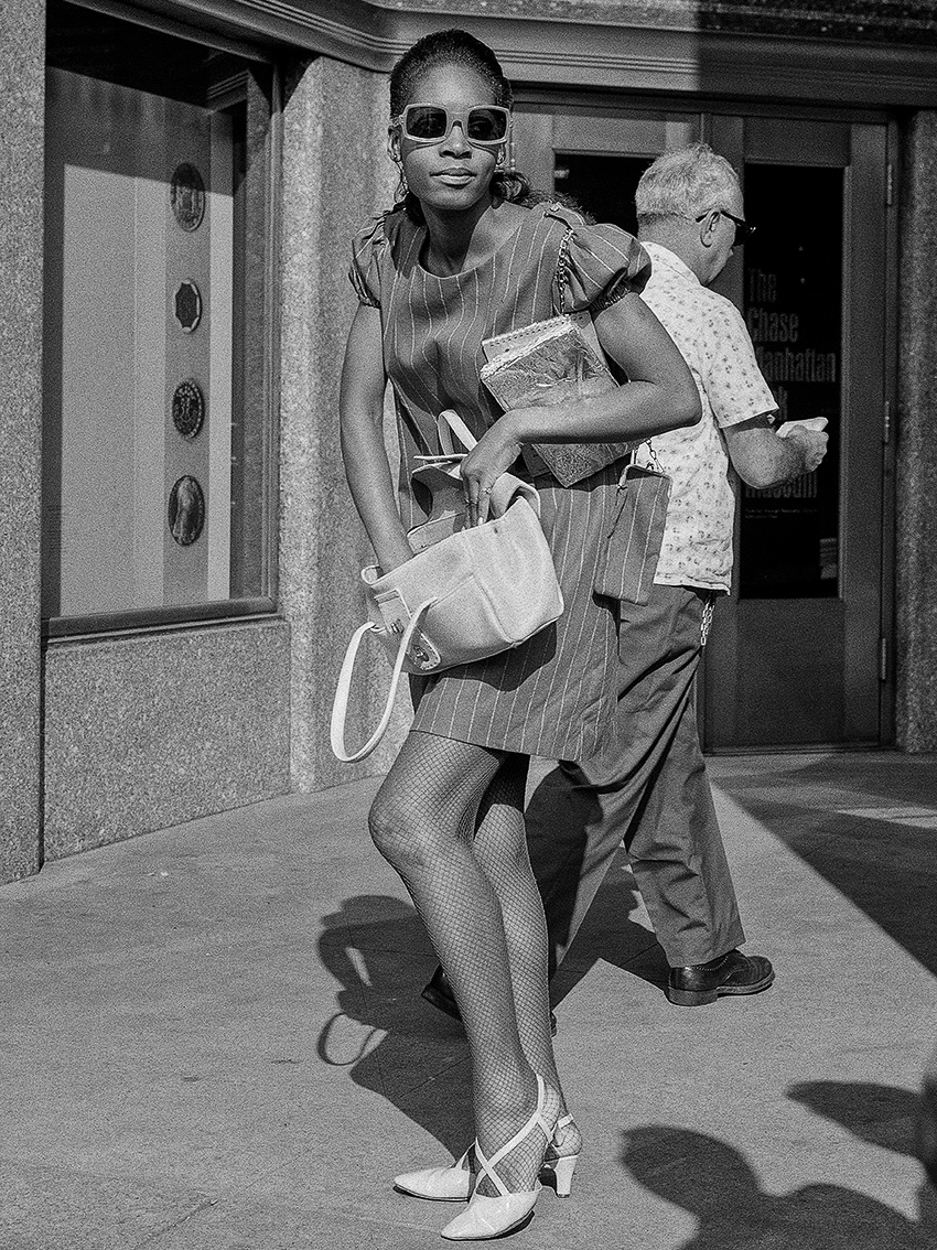 A woman walking down a sidewalk carrying a purse.
