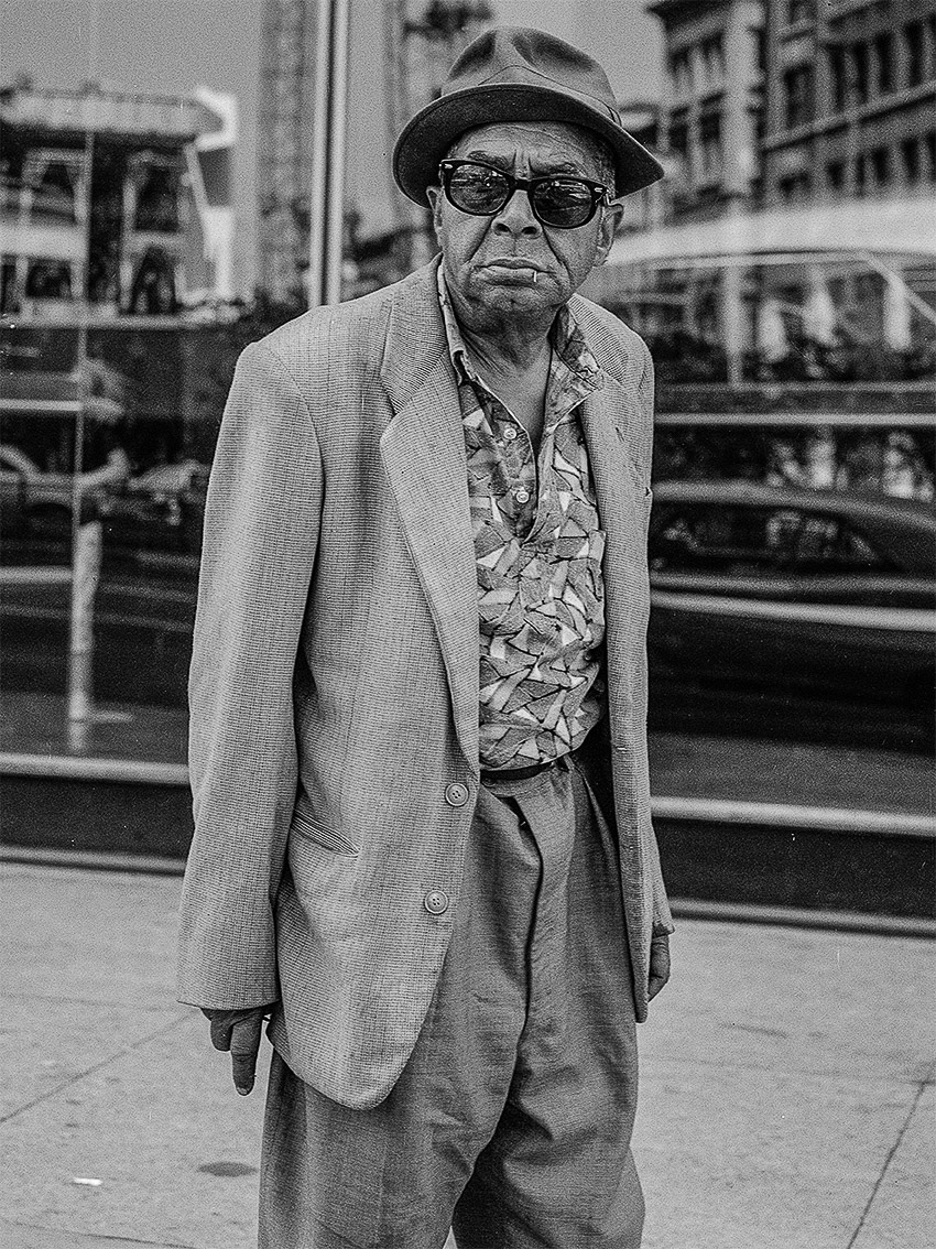 A man in a suit and hat standing on a sidewalk.