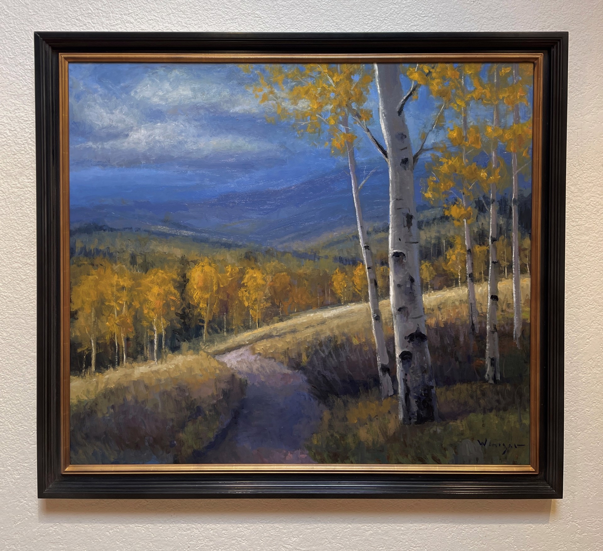 A serene autumn landscape featuring a winding path through golden aspen trees under a dramatic blue sky.