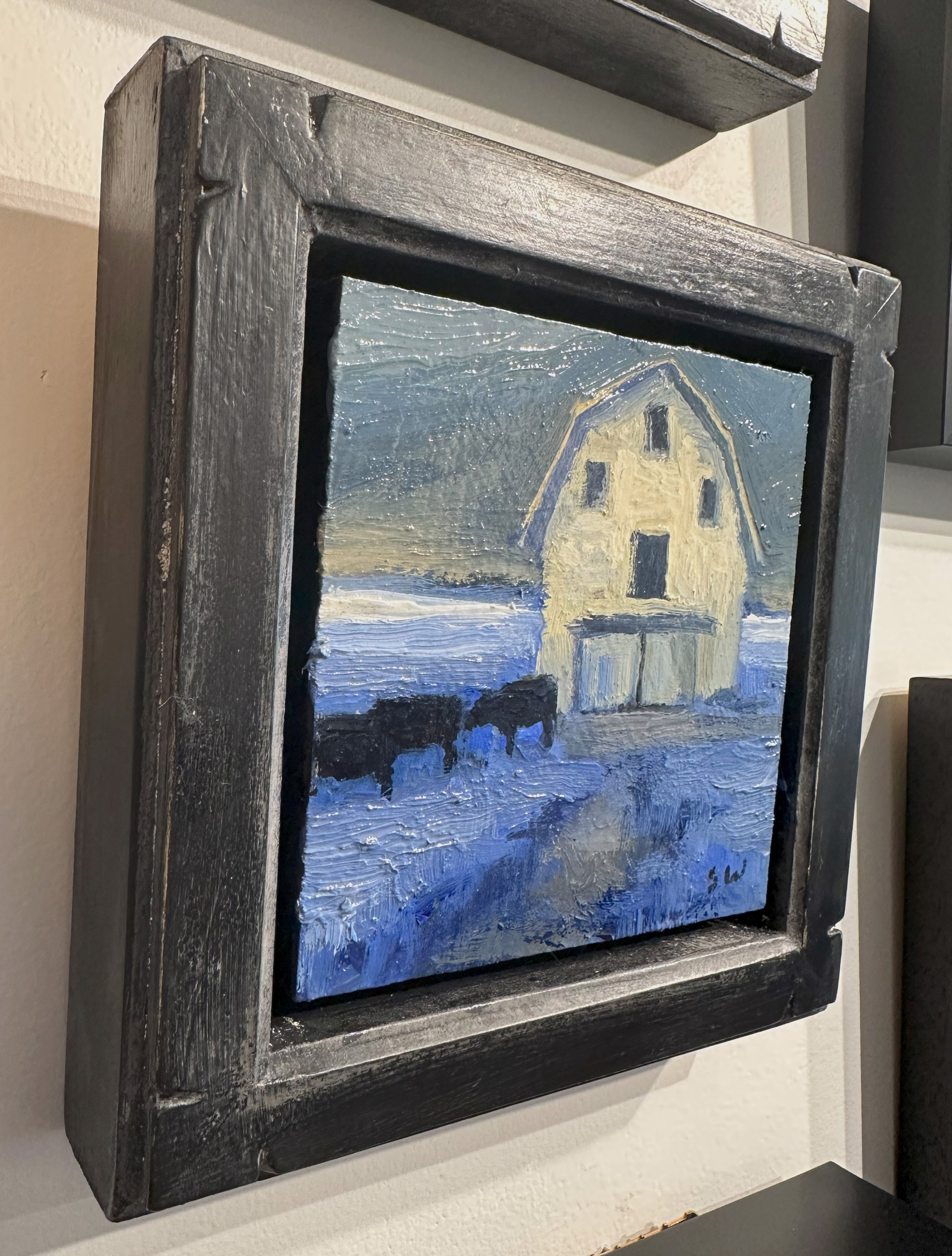 A painting of a white barn with two cows in the snow.