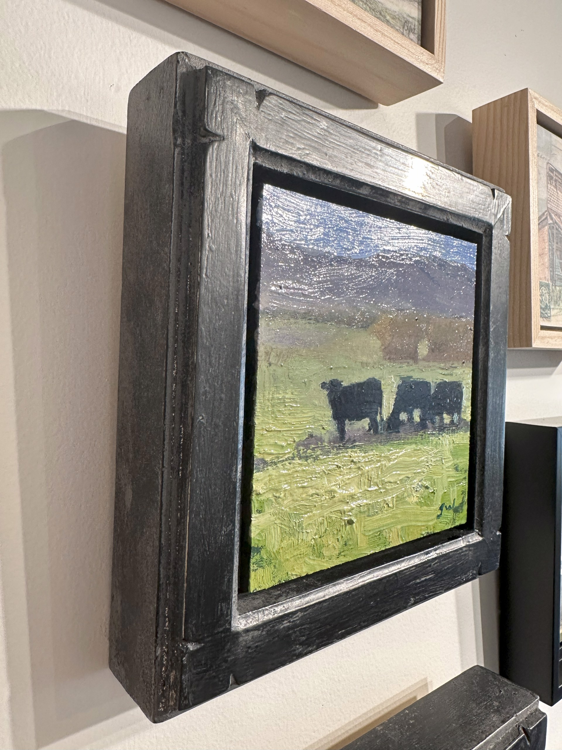 A painting of two cows grazing in a field.