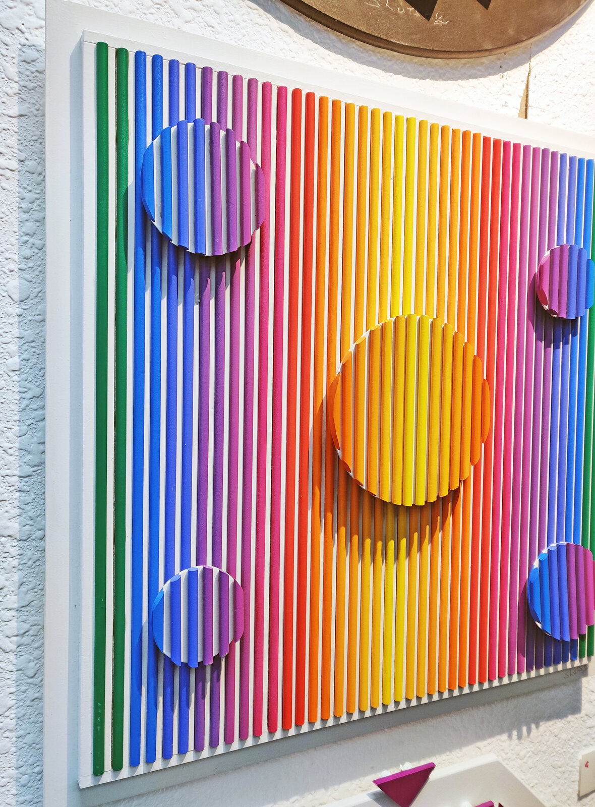 A painting of a rainbow colored striped wall with circles on it.