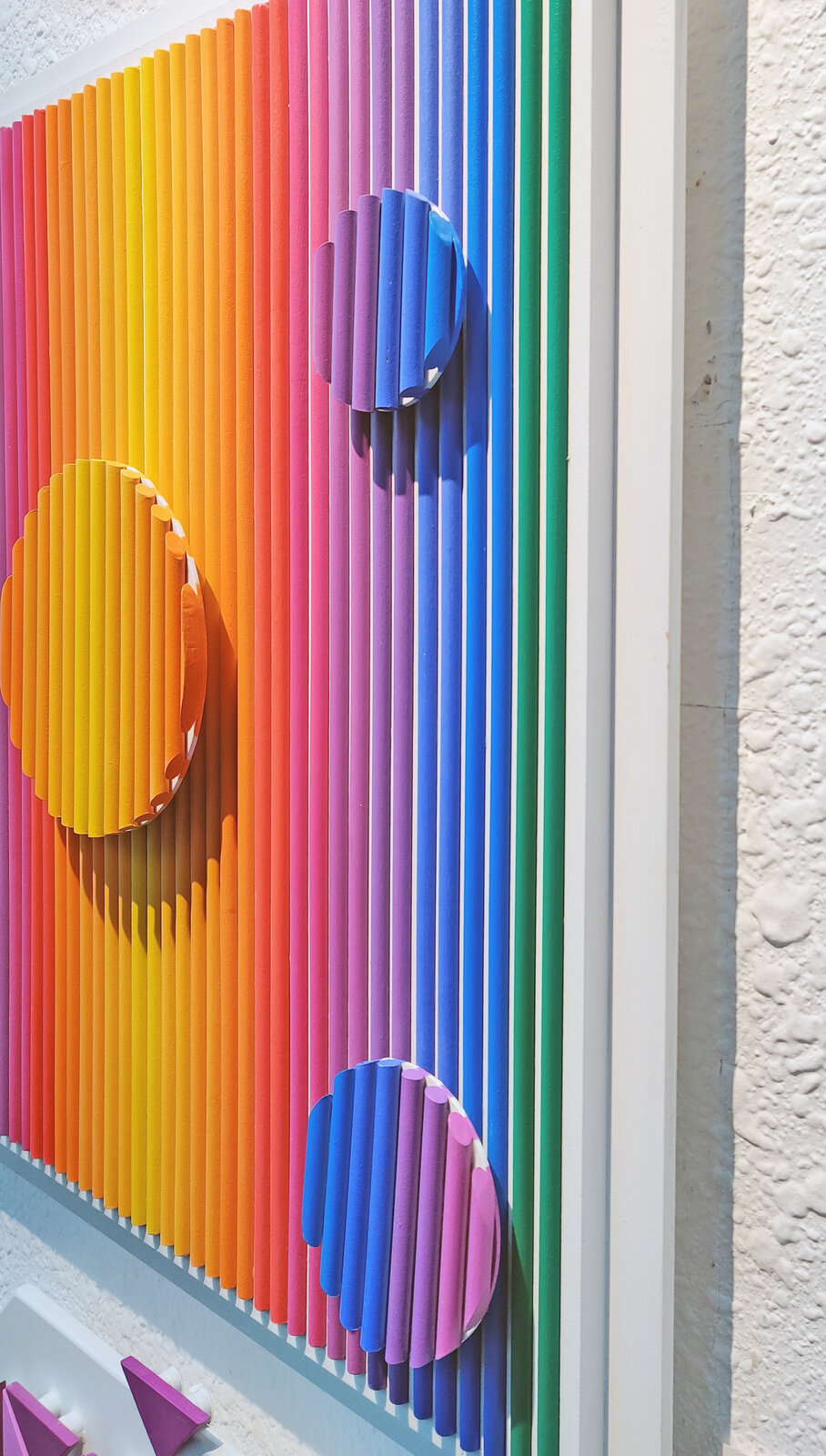 A painting of a rainbow colored striped wall with circles on it.