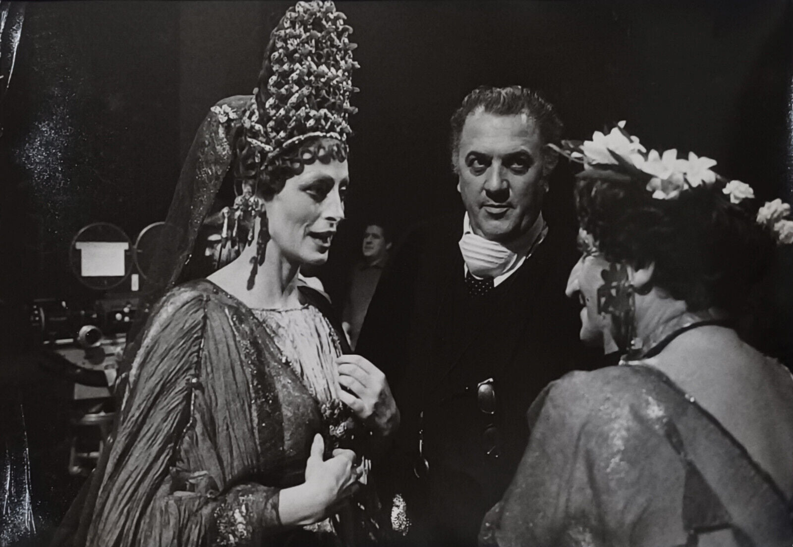 A black-and-white behind-the-scenes photograph capturing a moment of interaction between three figures in elaborate costumes.