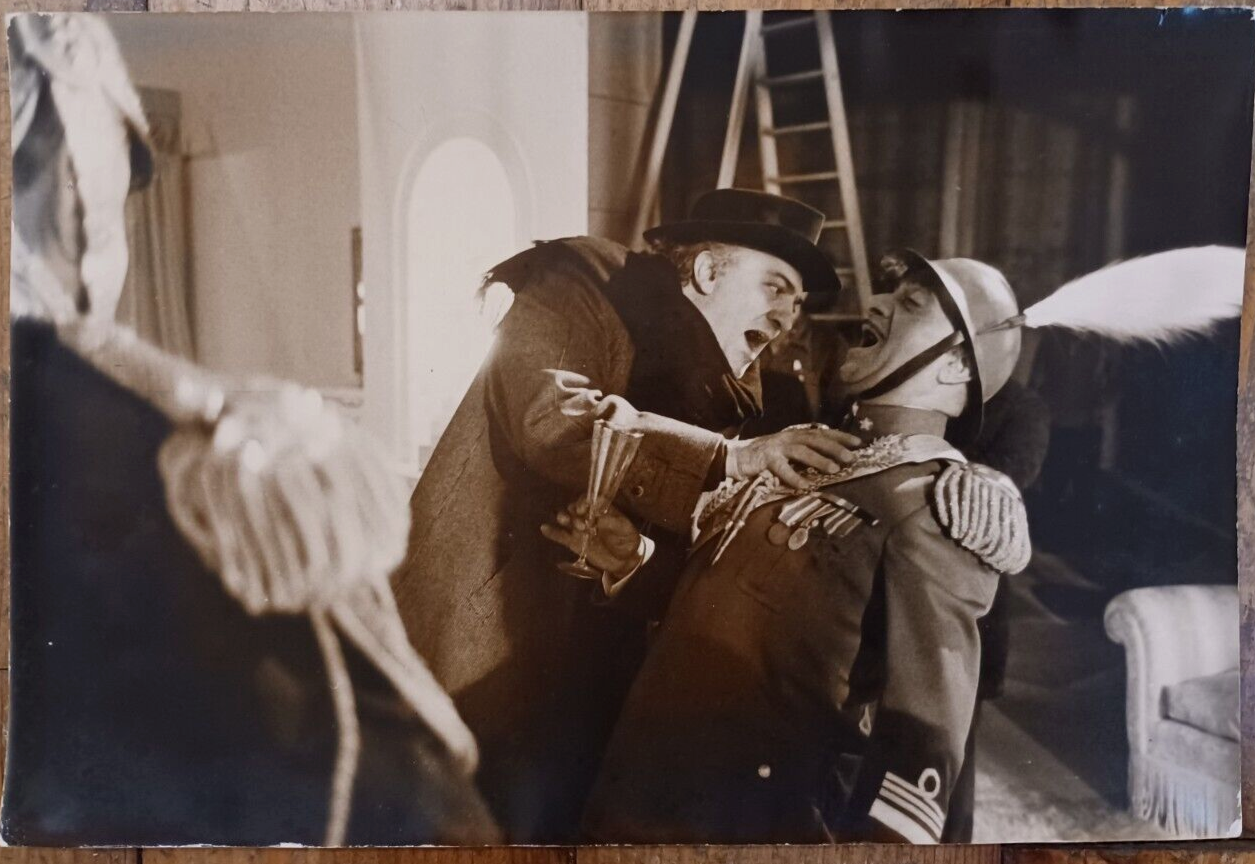 A dramatic, sepia-toned film still captures a tense confrontation between two figures in an interior setting.