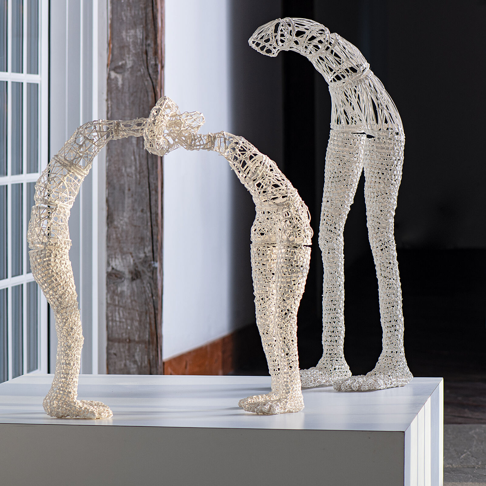 A white wireframe sculpture of a bowed figure stands on a pedestal.