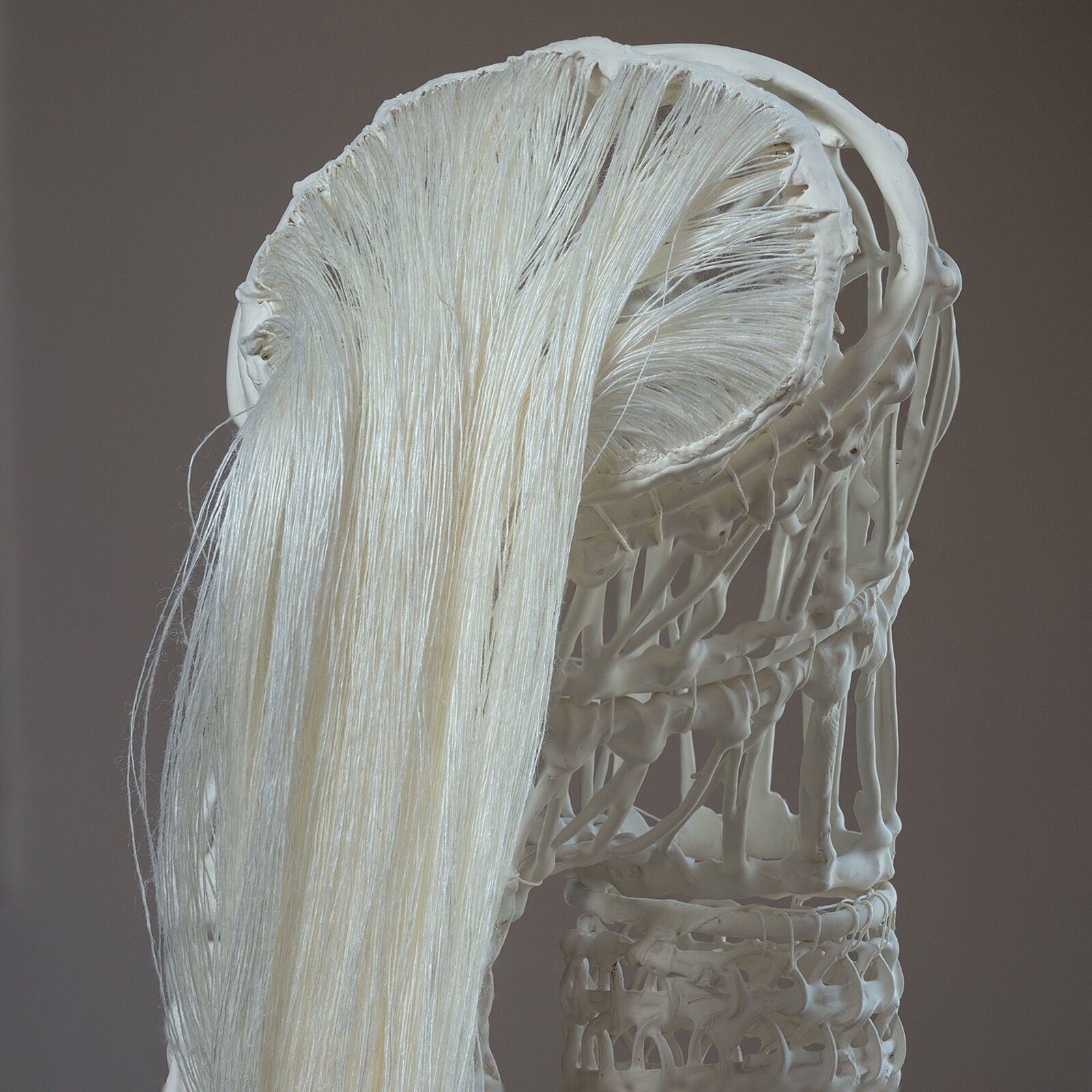 A white, crocheted sculpture resembling a stylized leg or boot standing on a dark wooden floor.