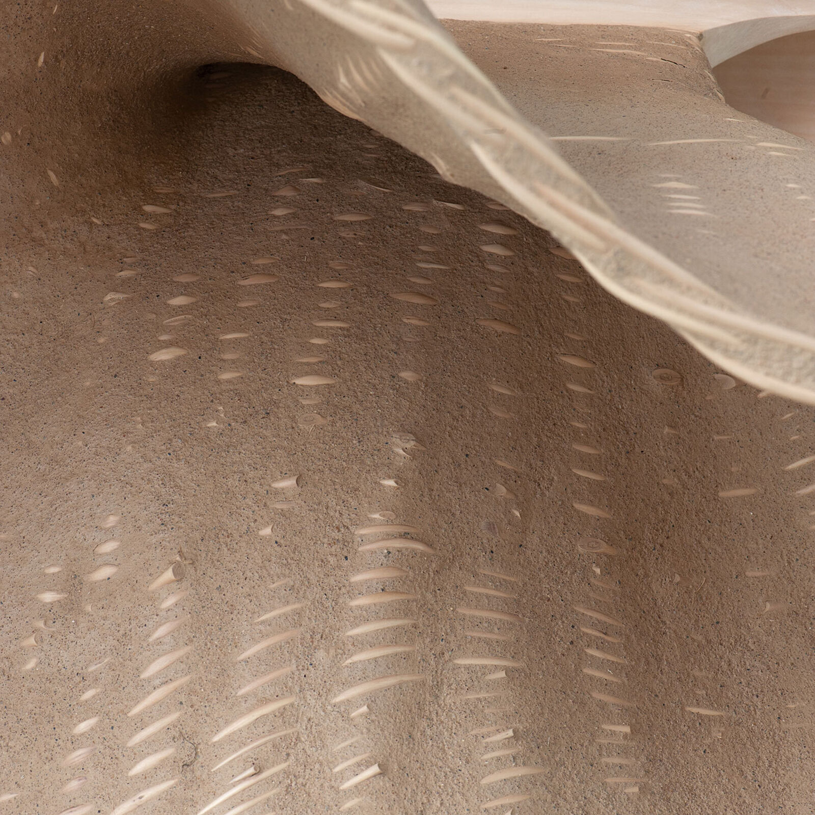 A wooden sculpture resembling a giant spoon resting on slate tiles.
