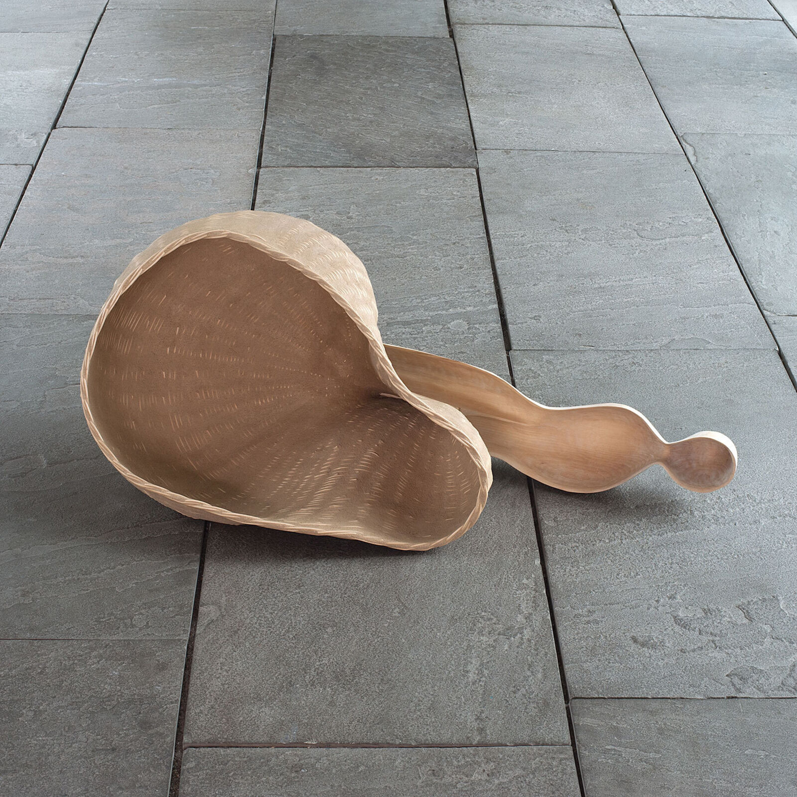 A wooden sculpture resembling a giant spoon resting on slate tiles.