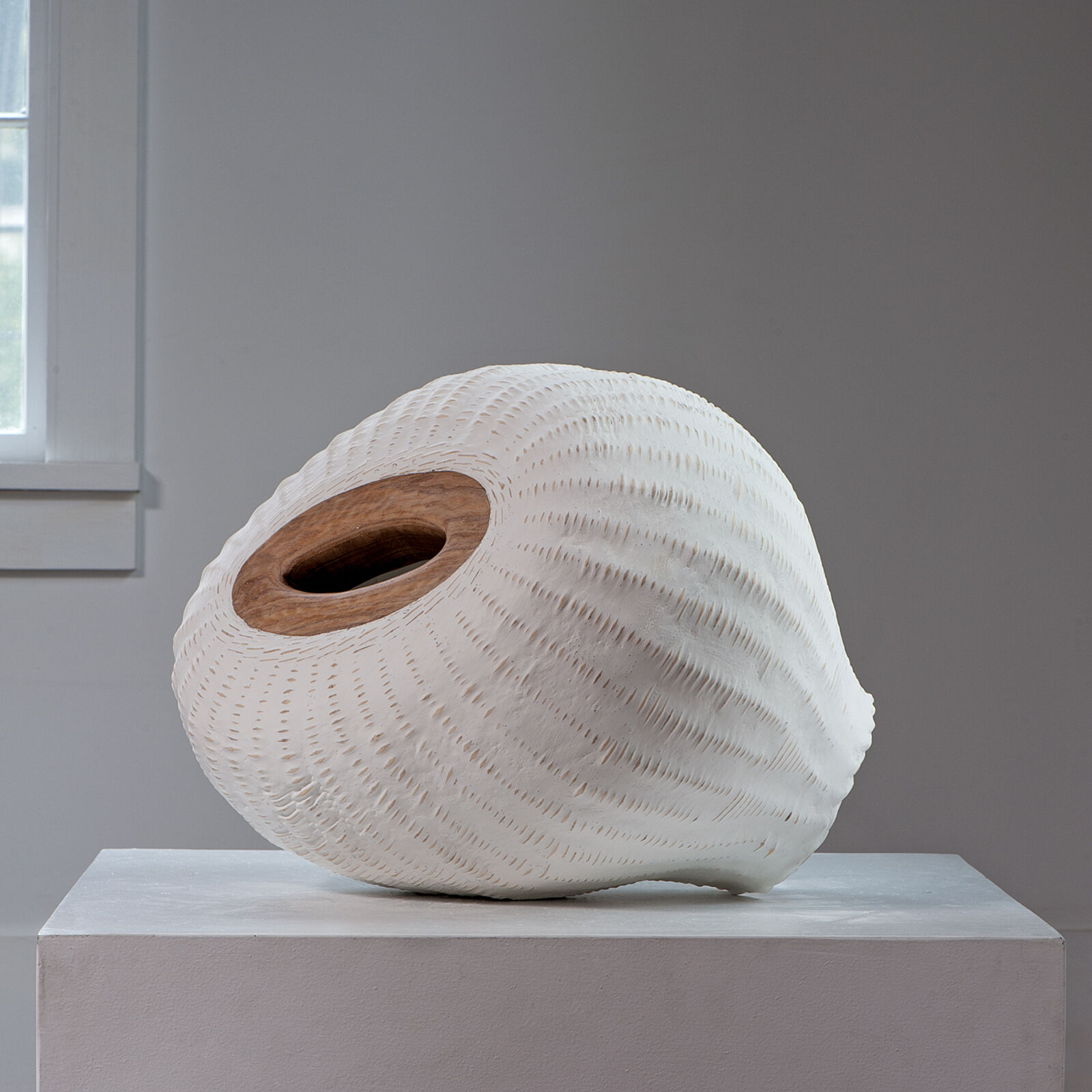 A textured white ceramic vessel with a wooden rim sits on a pedestal.