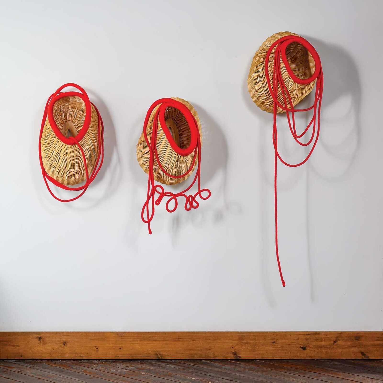 A minimalist wall installation featuring three woven baskets with vibrant red cords.
