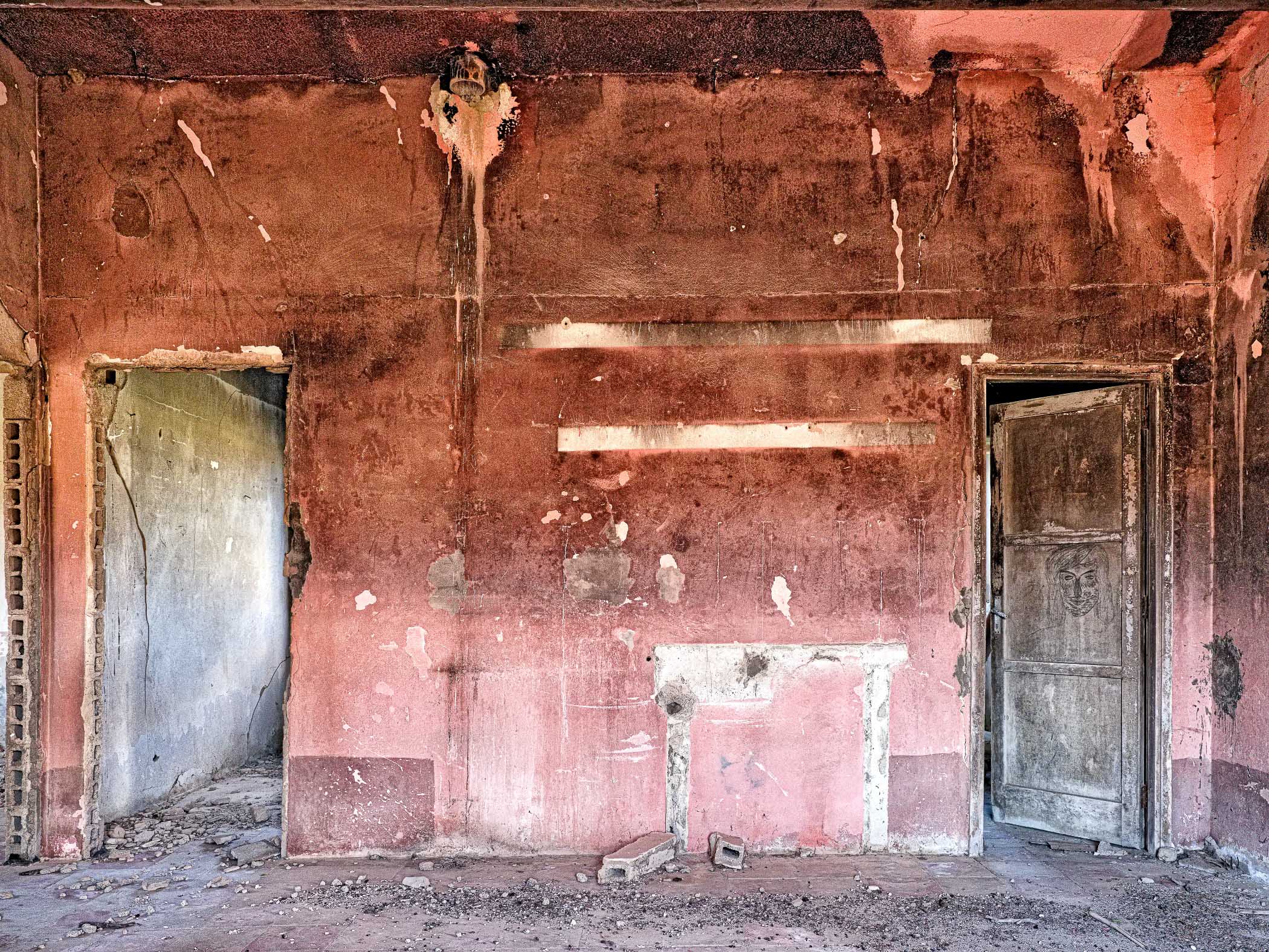 A room with peeling paint on the walls and two doors.