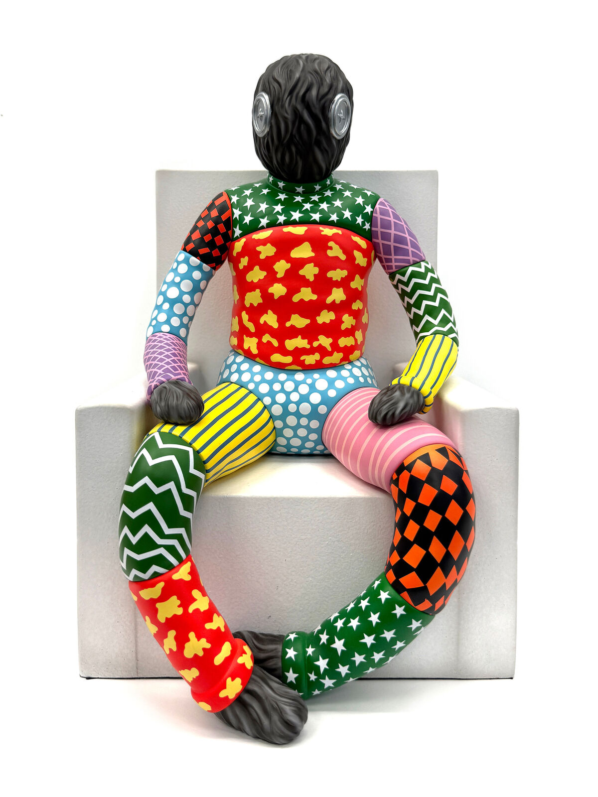 A colorful sculpture of a man sitting on a white cube.