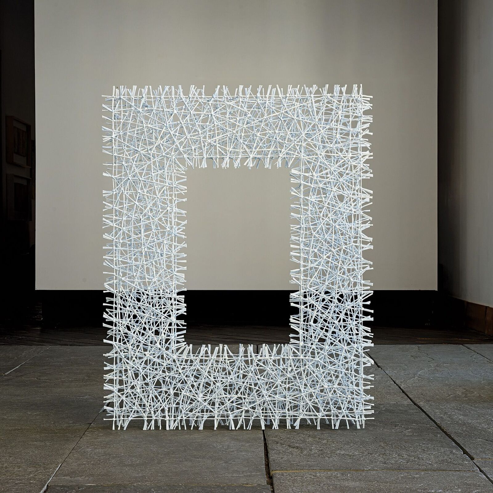 A white, frame-shaped sculpture made of tangled sticks or twigs.
