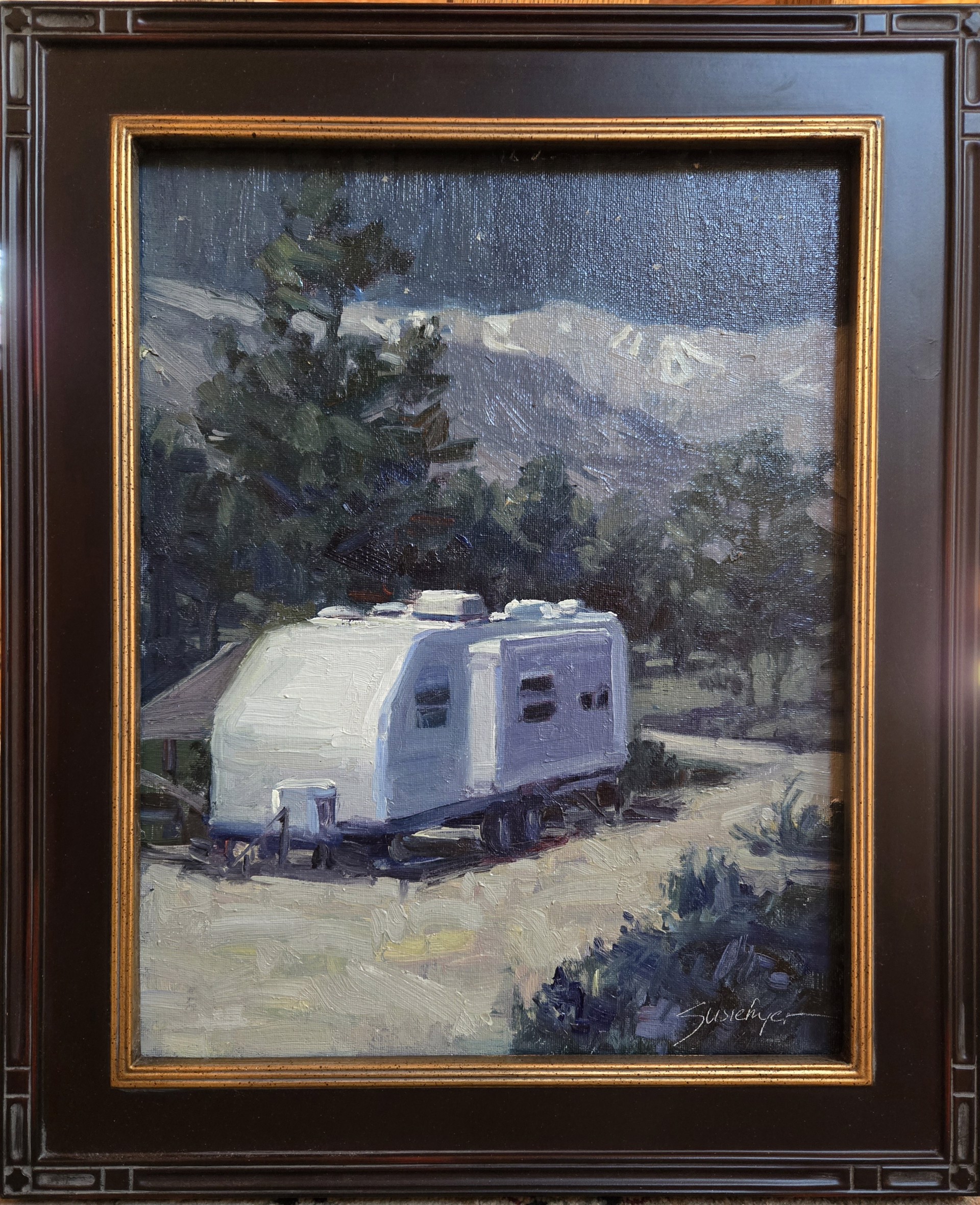 A white caravan rests on a dirt road in front of dark mountains under a starry night sky.