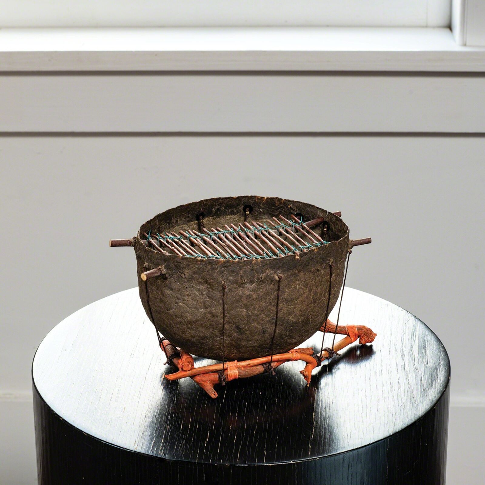 A rustic metal bowl with a grill-like top sits on an orange wooden stand atop a glossy black table.