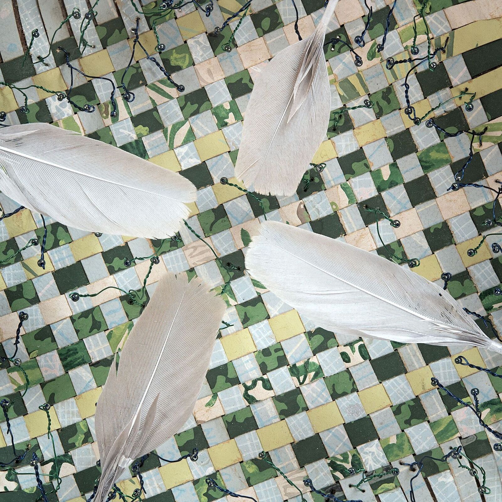 A handcrafted bowl with a mosaic interior and feathers rests on weathered wooden planks.