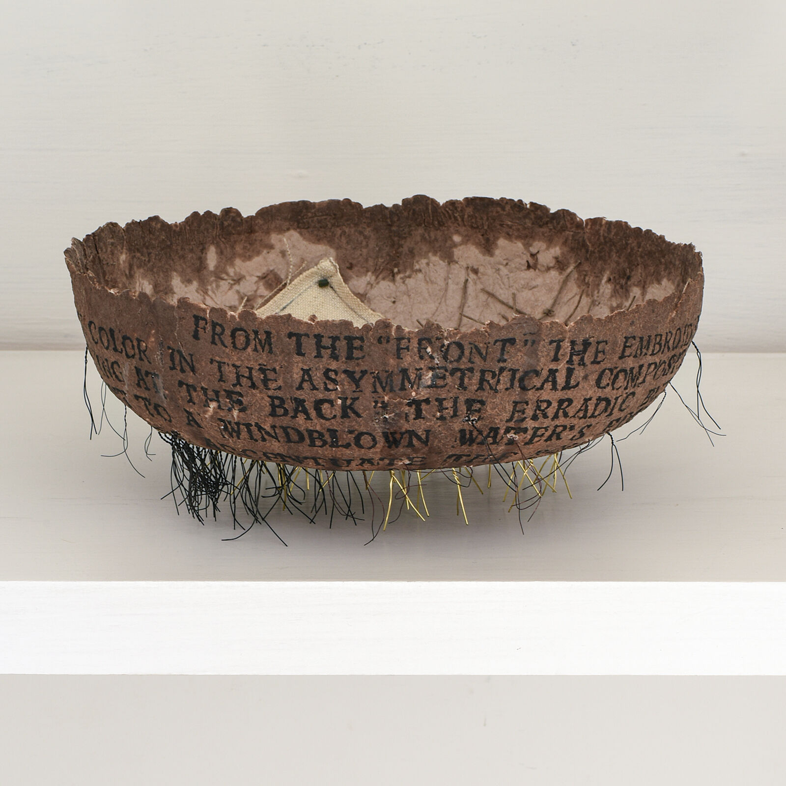 A brown bowl with writing on it sitting on a shelf.