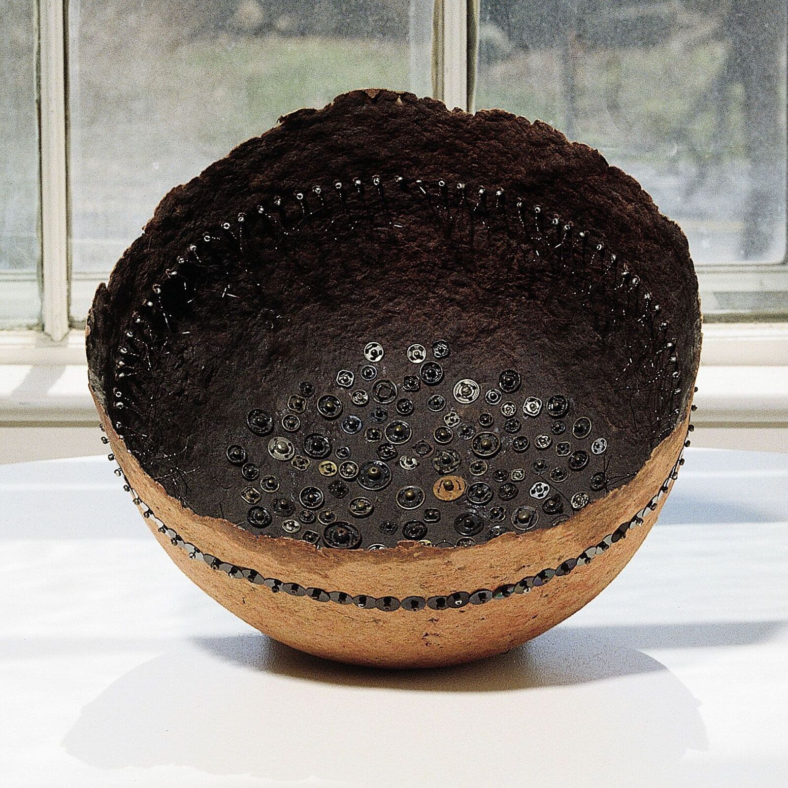 A textured bowl filled with dark soil, adorned with black sequins and wire.