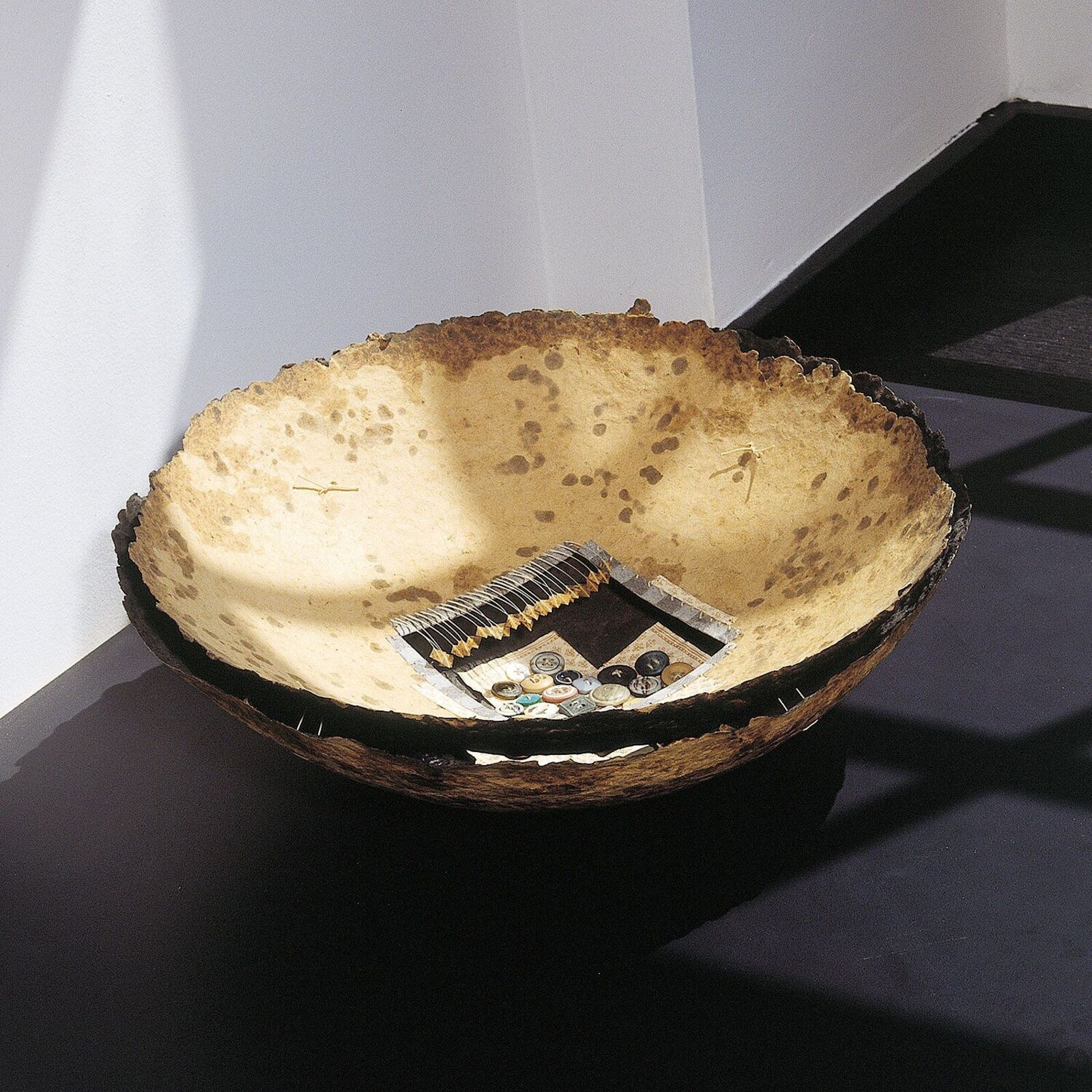 A rustic bowl with a collage of buttons and fabric inside.