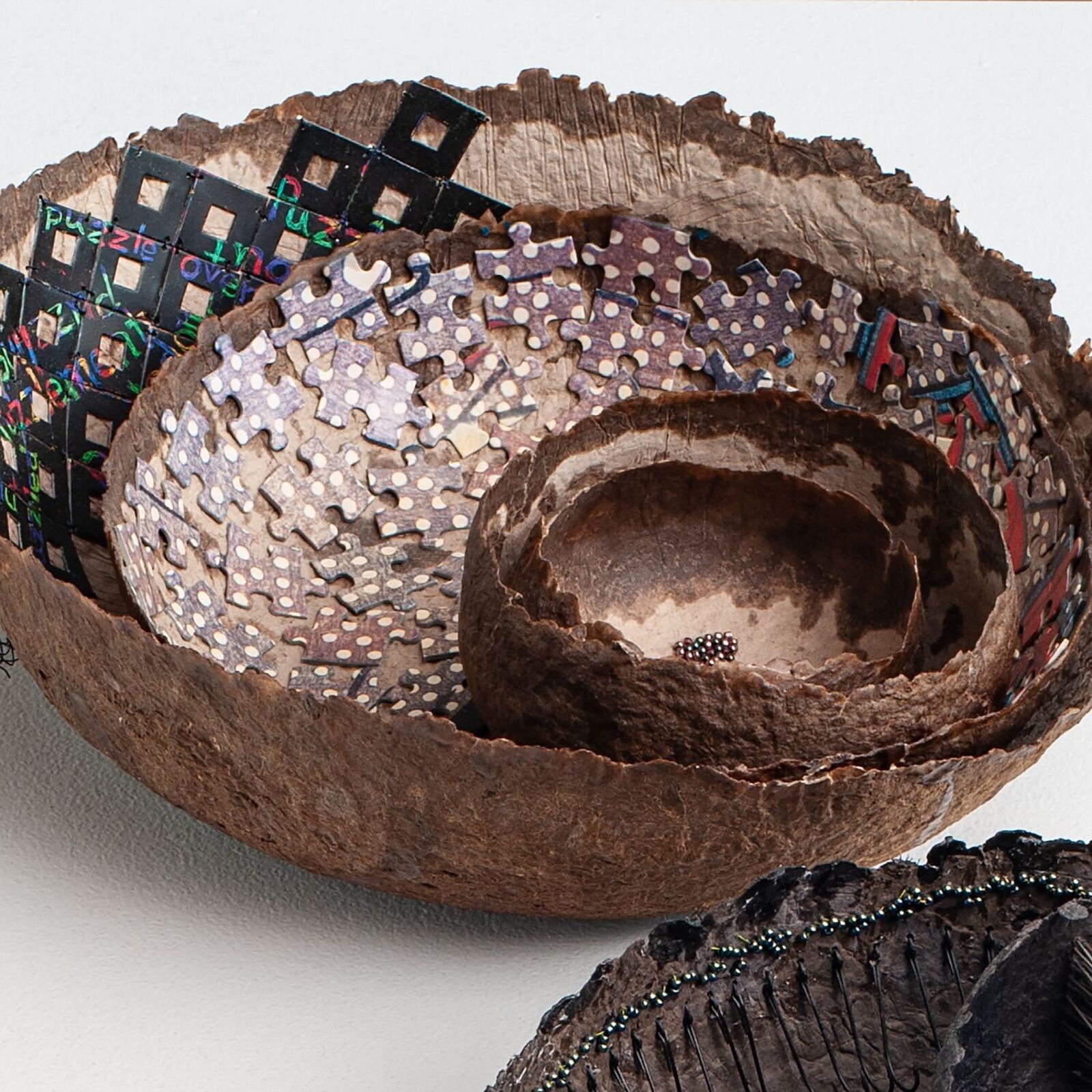 A nested sculpture of organic bowls filled with puzzle pieces and small beads.