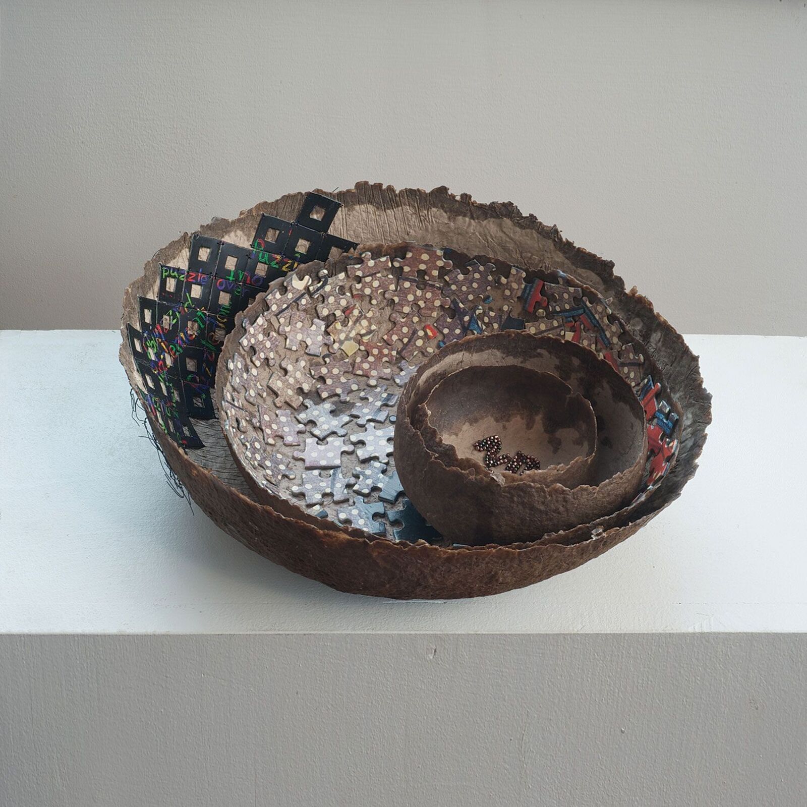 A nested sculpture of organic bowls filled with puzzle pieces and small beads.