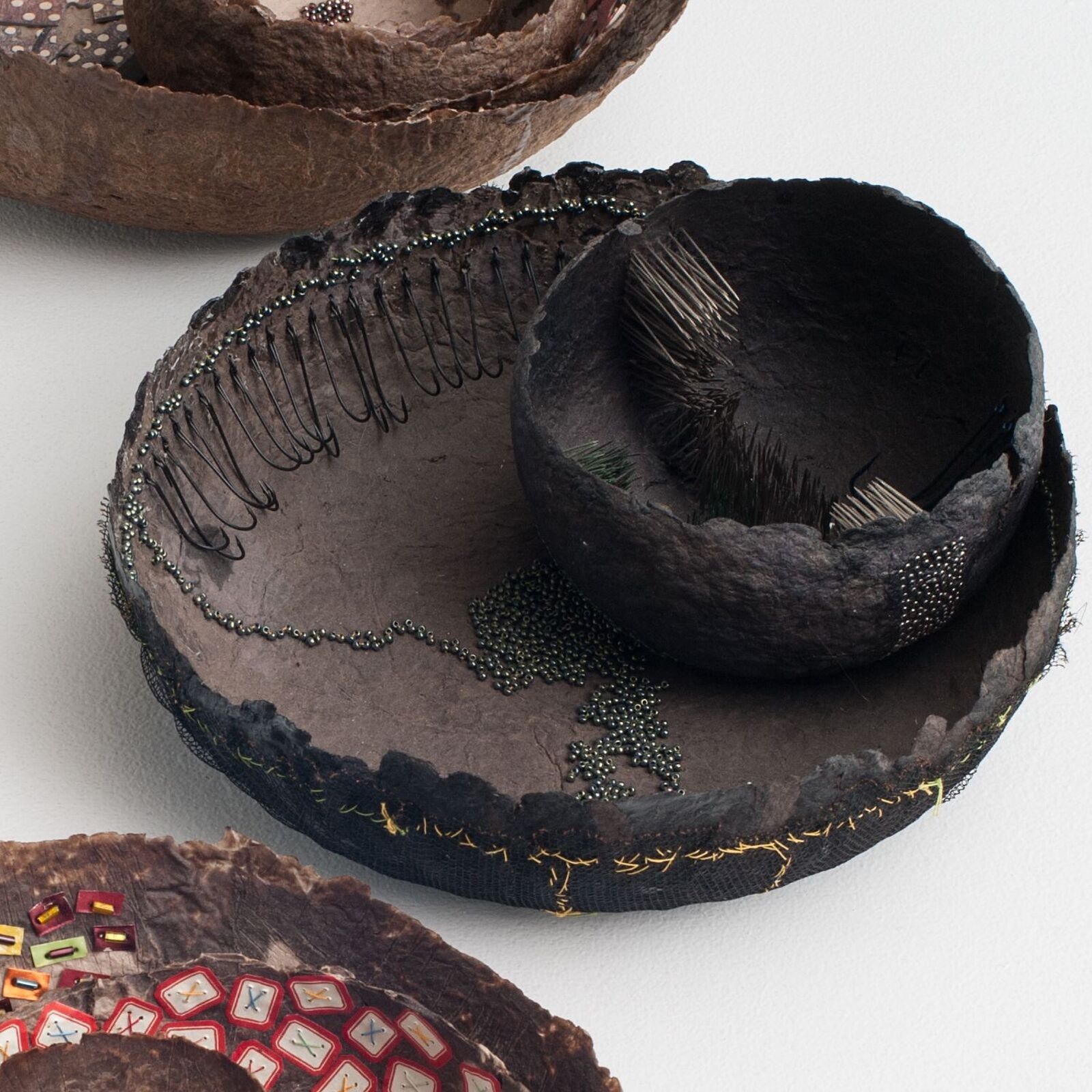 A high-angle view of a textured, bowl-like sculpture resting on a stone surface next to water.