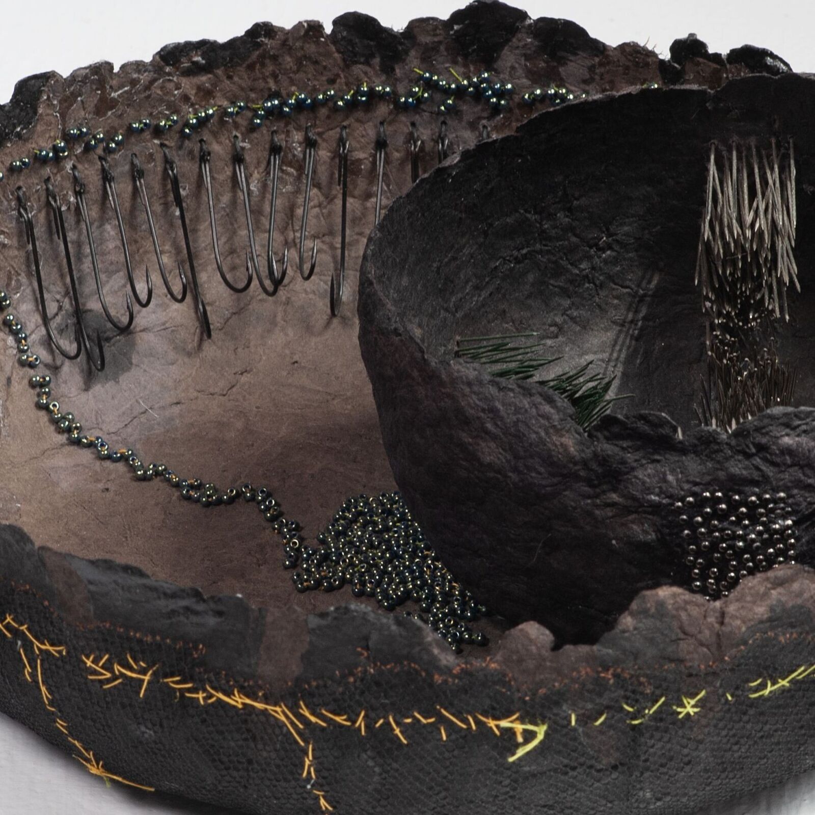 A high-angle view of a textured, bowl-like sculpture resting on a stone surface next to water.